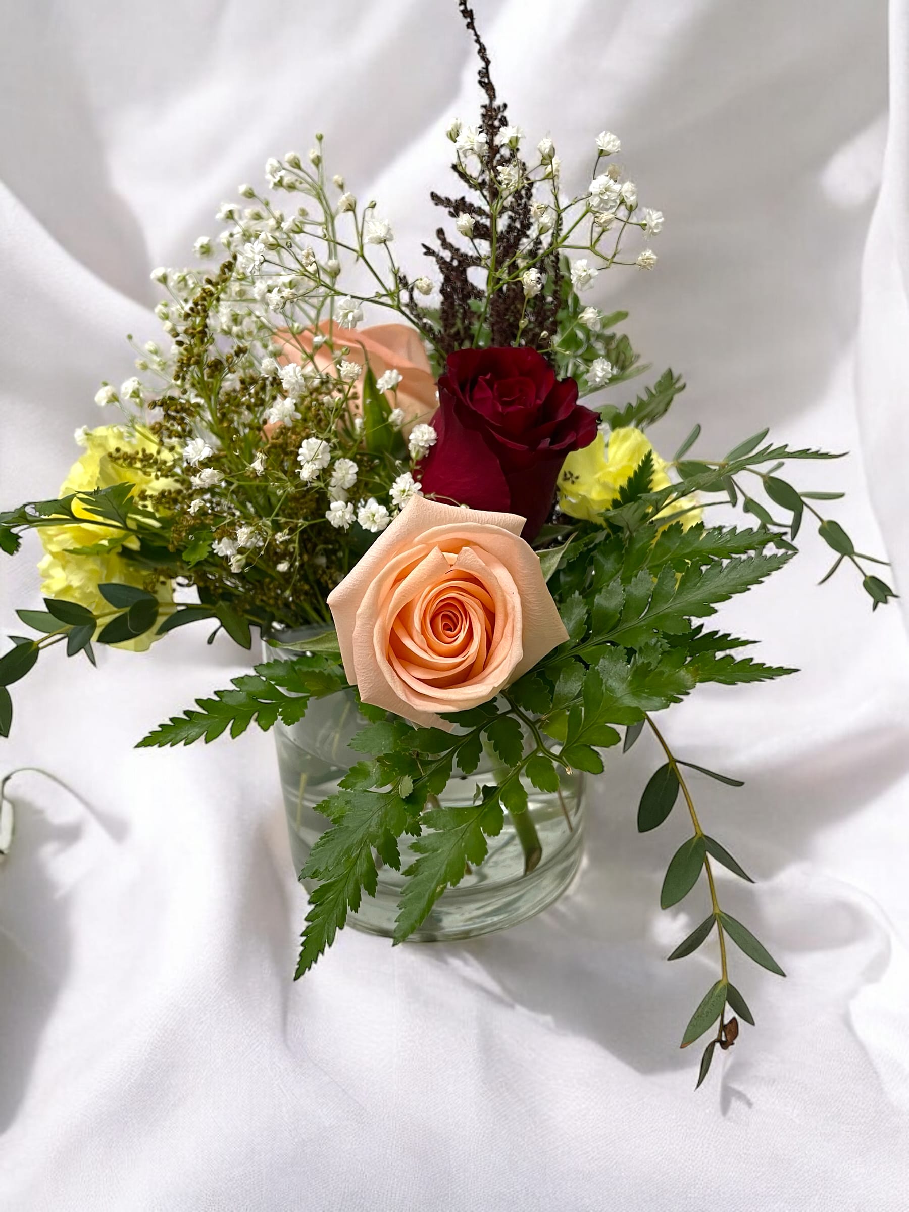 Graceful Bouquet  - A timeless blend of beauty and grace, this delicate floral arrangement features soft peach and deep red roses, complemented by airy baby's breath, vibrant yellow blooms, and lush greenery. Set in a simple glass vase, this arrangement brings a touch of natural elegance to any space. Whether as a gift or a centerpiece, it’s a perfect way to express love, appreciation, or just brighten someone’s day with the charm of fresh flowers.
