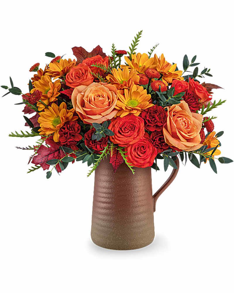 Terra Bloom Bouquet - Celebrate fall with The Terra Bloom Bouquet, a stunning mix of autumn flowers in a rustic stoneware pitcher. With rich orange and maroon hues, this seasonal arrangement is perfect for Thanksgiving décor or a warm harvest gift The Terra Bloom Bouquet includes fresh orange roses, orange spray roses, maroon miniature carnations, brown button spray chrysanthemums, and orange daisy spray chrysanthemums. Accented with parvifolia eucalyptus, grevillea, and preserved oak leaves, arranged in The food-safe Terra Bloom Pitcher