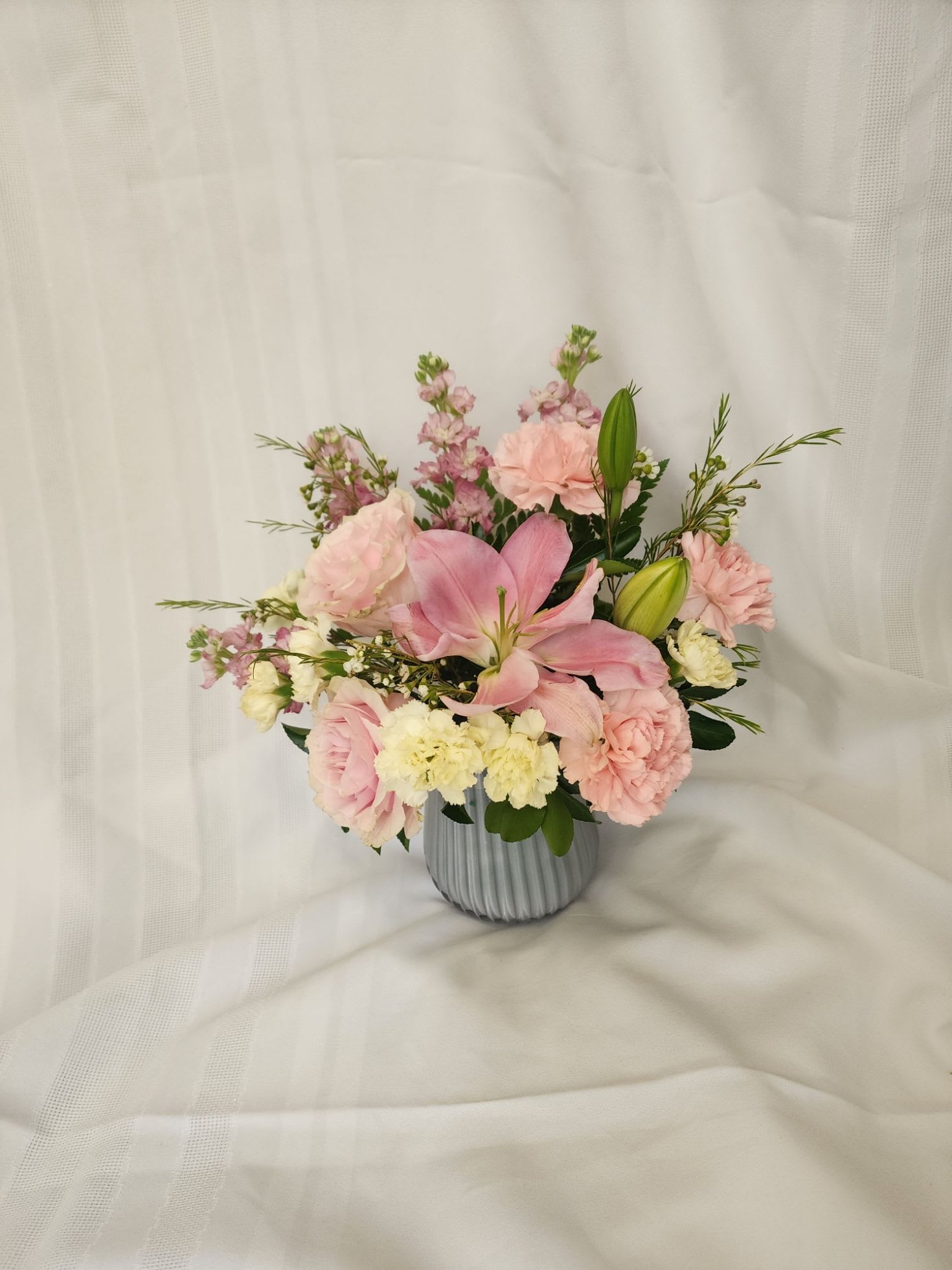 Blush Skies Blush Skies - Blush Skies is a dreamy arrangement that captures the delicate beauty of a soft sunrise. Featuring lush pink roses, graceful pink lilies, vibrant carnations, and fragrant stock, all nestled among rich greenery, this bouquet brings a sense of warmth and wonder. Presented in a charming light blue vase, it’s the perfect gift to brighten someone's day, celebrate a special moment, or simply add a touch of serene beauty to any space. Great arrangement to get your loved ones for Mother's Day