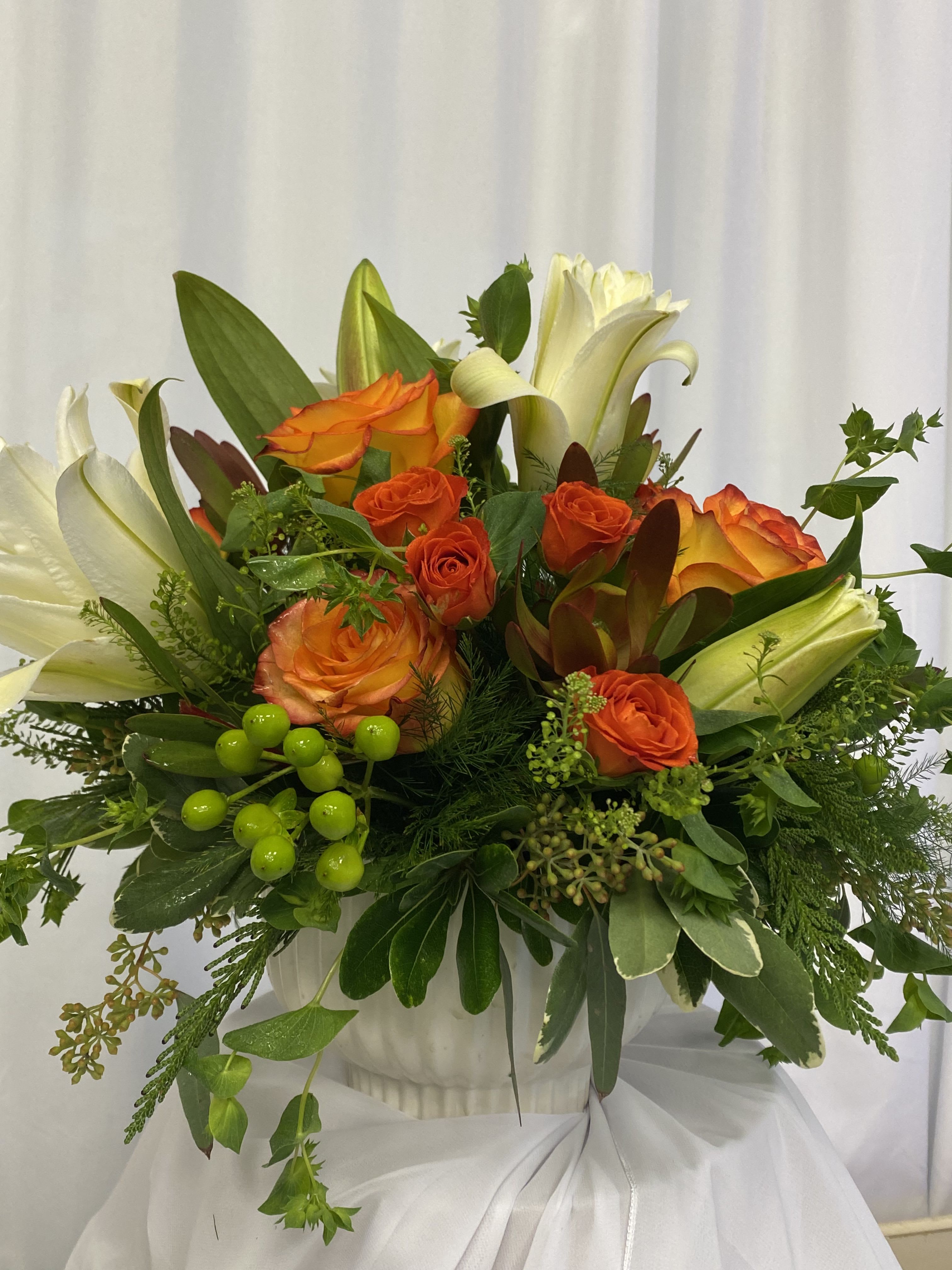 Sunset Serenity  - Embrace the calming beauty of our Sunset Serenity Arrangement, featuring a blend of pristine white lilies and vibrant orange roses, nestled in a sleek ceramic container. This low, compact arrangement exudes a peaceful elegance, reminiscent of a tranquil sunset over a serene landscape. Perfect for any occasion or as a thoughtful &quot;just because&quot; gift, our Sunset Serenity Arrangement is a stunning addition to any space.