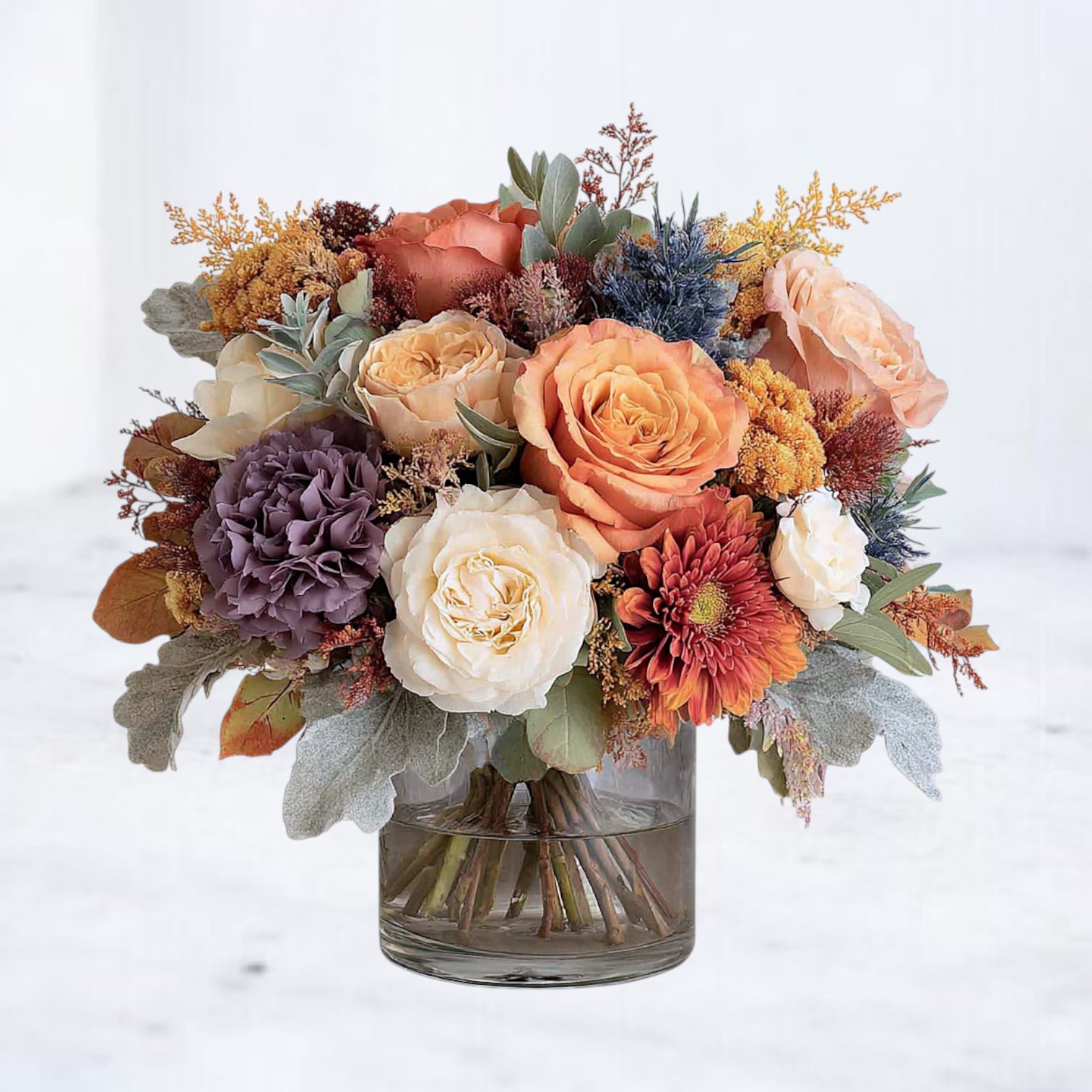 Fall Shimmer Bouquet Fall Shimmer Bouquet - The Fall Shimmer Bouquet is a warm and inviting fall arrangement featuring peach and orange roses, creamy white blooms, dusty lavender accents, and seasonal textures. Designed in a modern glass vase with soft greenery, this bouquet captures the richness of the season with elegance and depth. Perfect for fall birthdays, Thanksgiving gatherings, or as a romantic seasonal gift, it brings cozy sophistication to any setting. Available for same-day flower delivery in Houston and surrounding areas, the Fall Shimmer Bouquet is a timeless expression of autumn beauty.