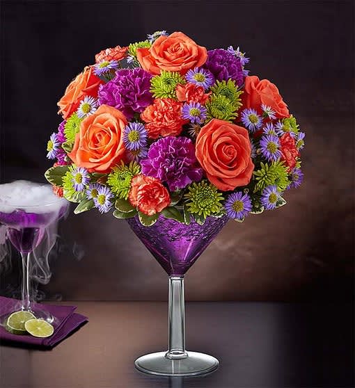 Shocktail Martini Bouquet Shocktail Martini Bouquet - We’re shaking things up for Halloween with our shocking cocktail creation! It’s the perfect mix of vibrant orange and purple blooms inside an oversized margarita plastic glass. Colorful and totally unique, it’s sure to make Halloween parties and fall celebrations straight-up fun. This Floral drink will be created in an oversized plastic margarita glass vase. All-around arrangement with purple carnations and monte casino, orange roses and mini carnations, Athos poms; accented with assorted greenery and a plastic spider on top. Artistically hand-designed in an over sized acrylic martini glass filled with purple crystal gel; We hand-design each arrangement, so colors and varieties may vary due to local availability