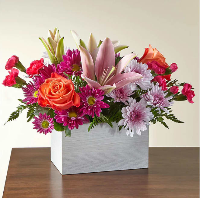 Light of My Life Box Bouquet - From life's big moments to sweet just because sentiments, the Light of My Life Box Bouquet is designed to celebrate your loved ones any day of the year. RSVP'd to the party are hot pink carnations, orange roses, lavender cushion poms and lush greens.  Please Note: The bouquet pictured reflects our original design for this product. While we always try to follow the color palette, we may replace stems to deliver the freshest bouquet possible, and we may sometimes need to use a different vase.