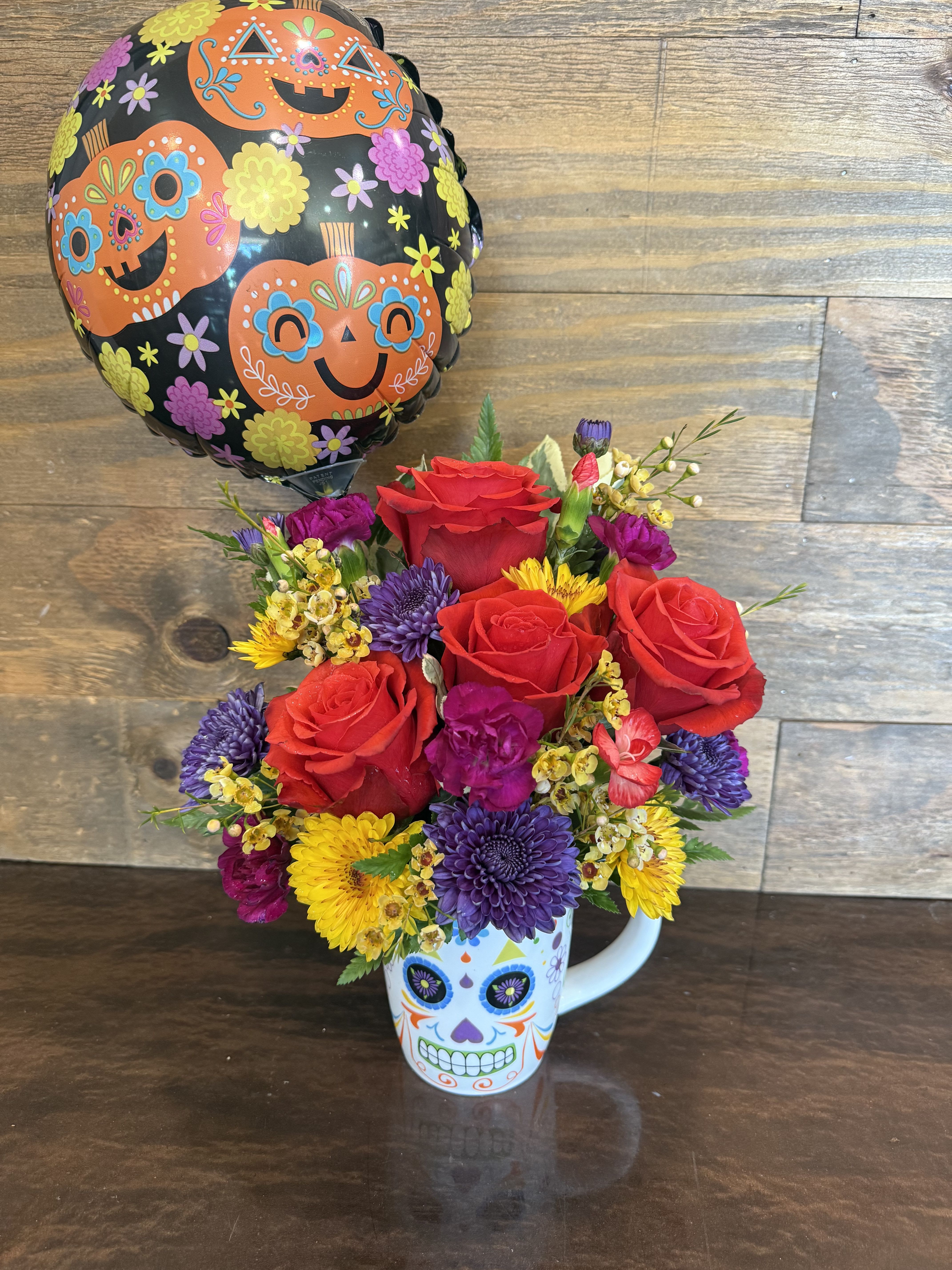 Fiesta Blooms  - This vibrant arrangement bursts with life and color, featuring bold roses, rich purple mums, and playful fuchsia carnations. Housed in a festive Día de los Muertos sugar skull mug, it beautifully blends celebration and tradition. Perfect as a lively centerpiece or a thoughtful gift, Fiesta Blooms brings joy, culture, and a splash of color to any space.