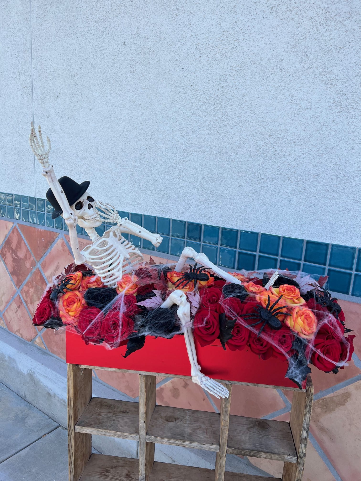 Awaken - Set the scene for a spine-chilling soirée with this long and low Halloween bouquet, bursting in bold shades of red, black, and fiery orange. Nestled among the dramatic blooms is a 3-foot skeleton, tangled in eerie spider webs and crawling with creepy spiders. Perfect as a haunted table centerpiece or a statement decoration, this arrangement is where beauty meets the macabre.