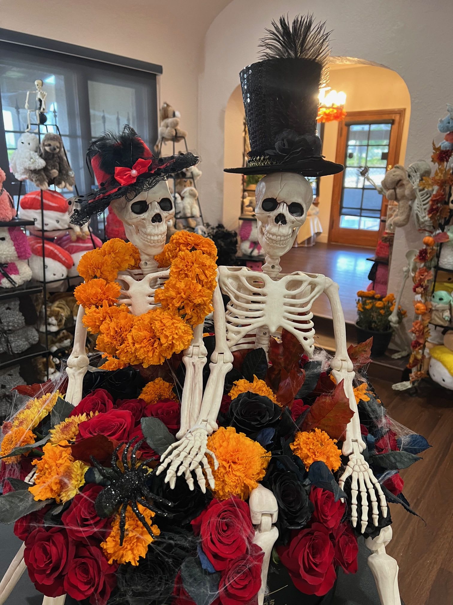 Eternal Love - Where passion meets the paranormal. This striking Halloween arrangement overflows with red, black, and orange roses, carnations, and poms — a fiery palette symbolizing love. Twisting through the blooms are eerie spider webs, crawling spiders, and a pair of 2–3 ft skeletons locked in an eternal embrace. Bold, gothic, and unforgettable, Eternal Love is the perfect fusion of romance and the macabre.