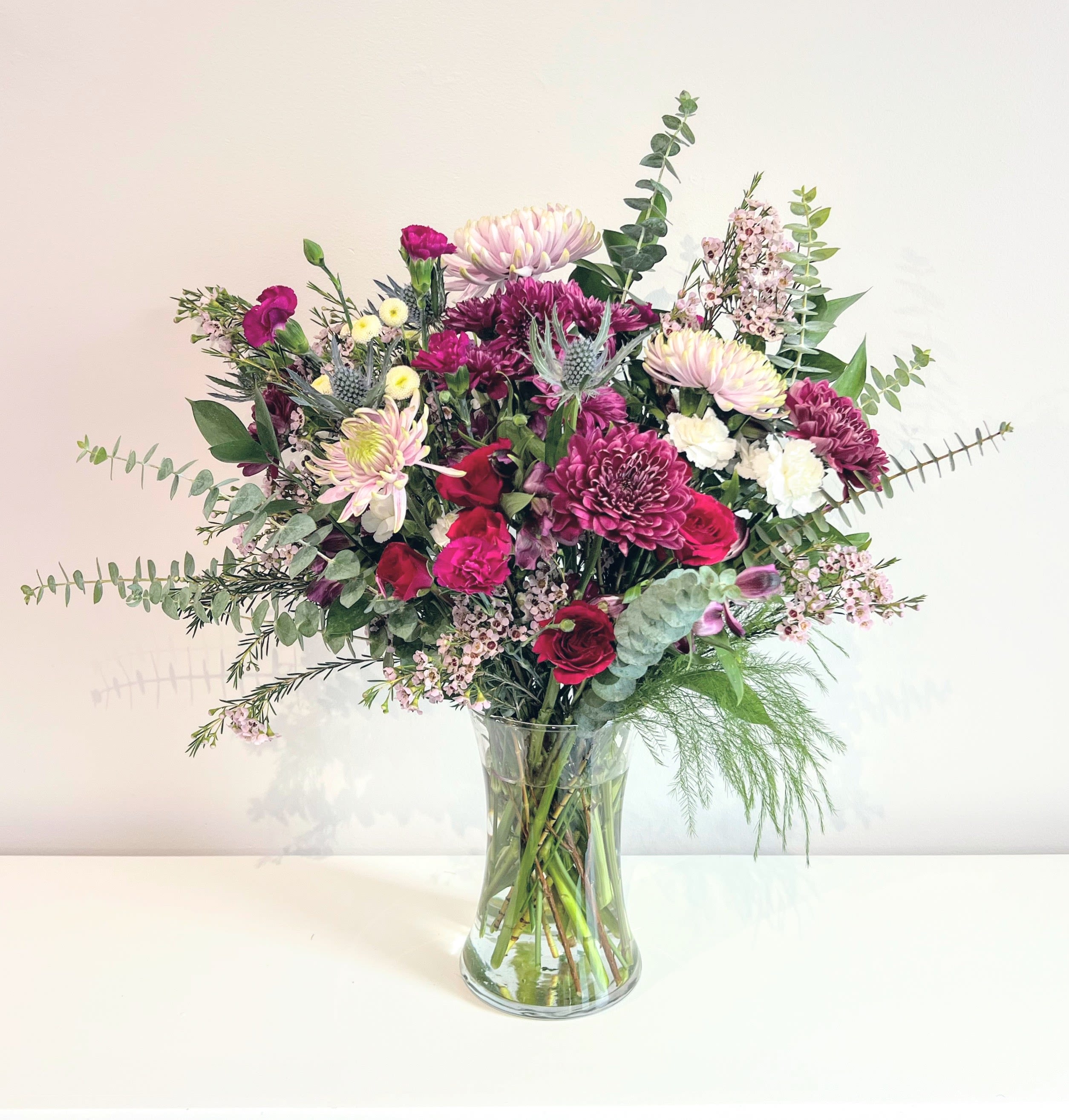 Something Wild - A wildly lush bouquet showcasing the best seasonal blooms in burgundy, purple, lavender &amp; white with a pops of red. Accented with lots of fragrant spiral eucalyptus &amp; dark greens. Arranged tall &amp; natural in a clear glass gathering vase. It's the perfect floral gift for any special occasion.  Measures approx. 19&quot; tall and 16&quot; wide Orientation: All around