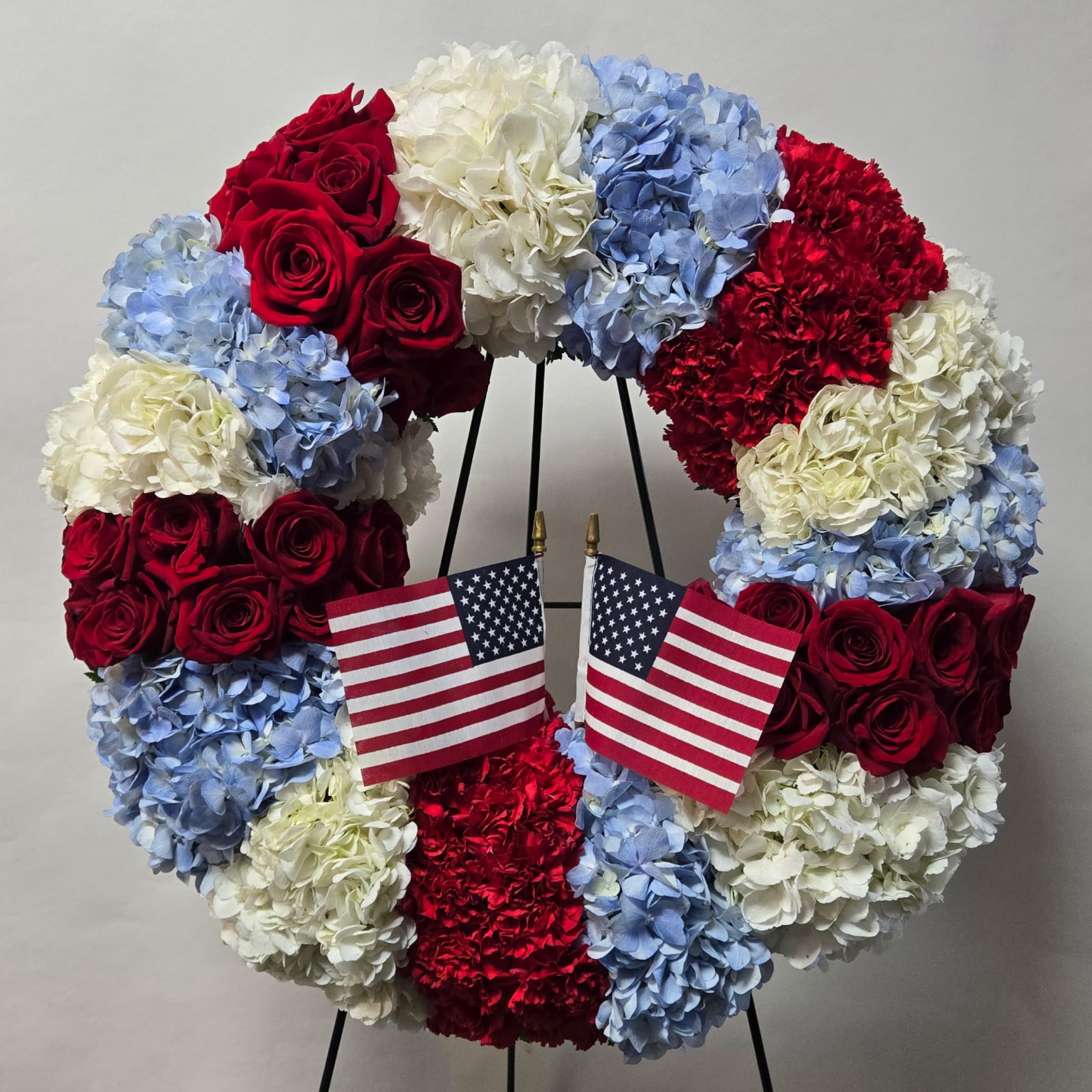 Patriot Honor Wreath Patriot Honor Wreath - 18" Wreath Includes Red Roses, Red Carnations, White Hydrangeas and Blue Hydrangeas with 2 flags. Or as Similar as Possible.