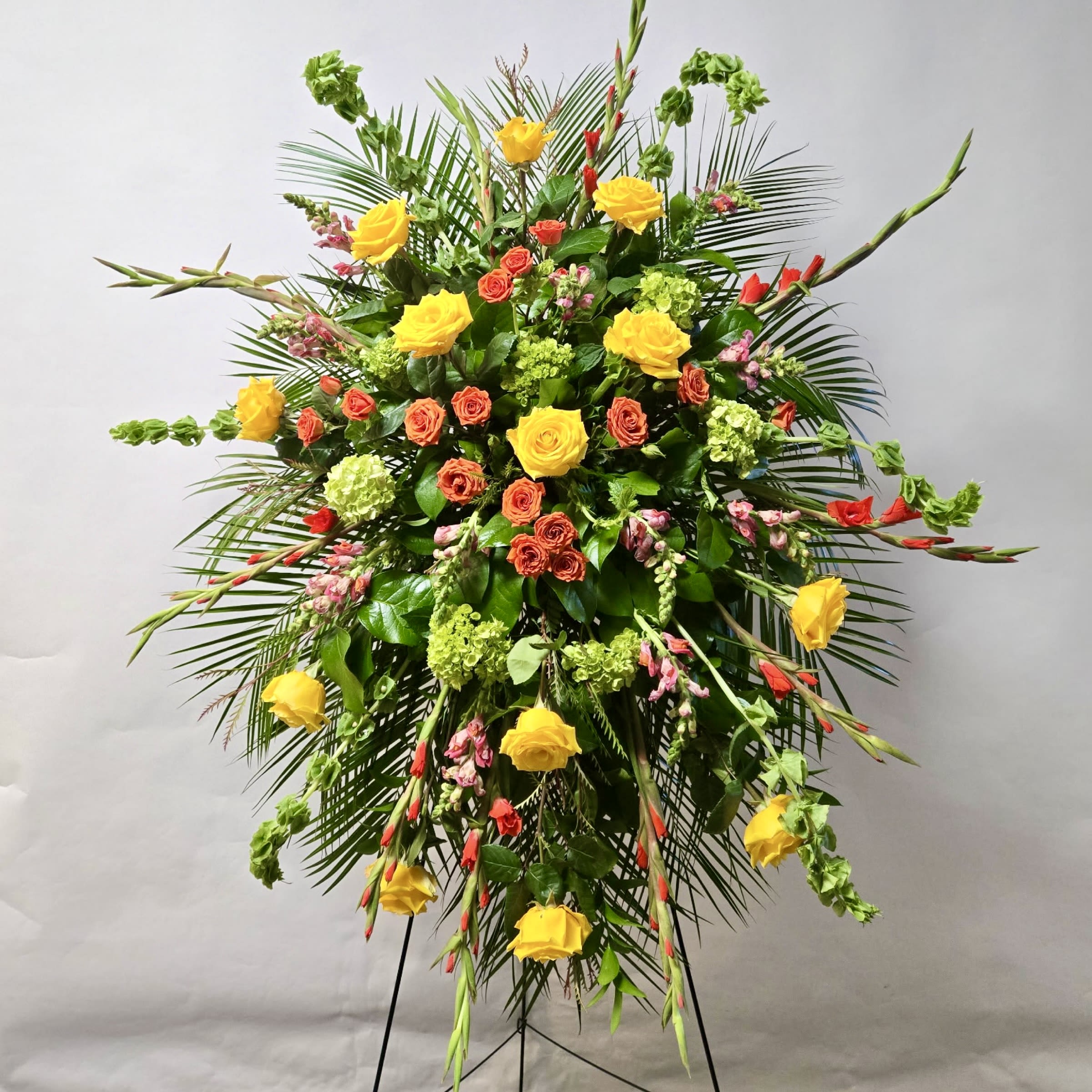 Sunlit Remembrance Standing Spray Sunlit Remembrance Standing Spray - This Standing Spray Includes Orange Gladiolas, Yellow Roses, Light Pink Snapdragons, Bells of Ireland, Orange Spray Rose's and Green Mini Hydrangea. Or as Similar as Possible.