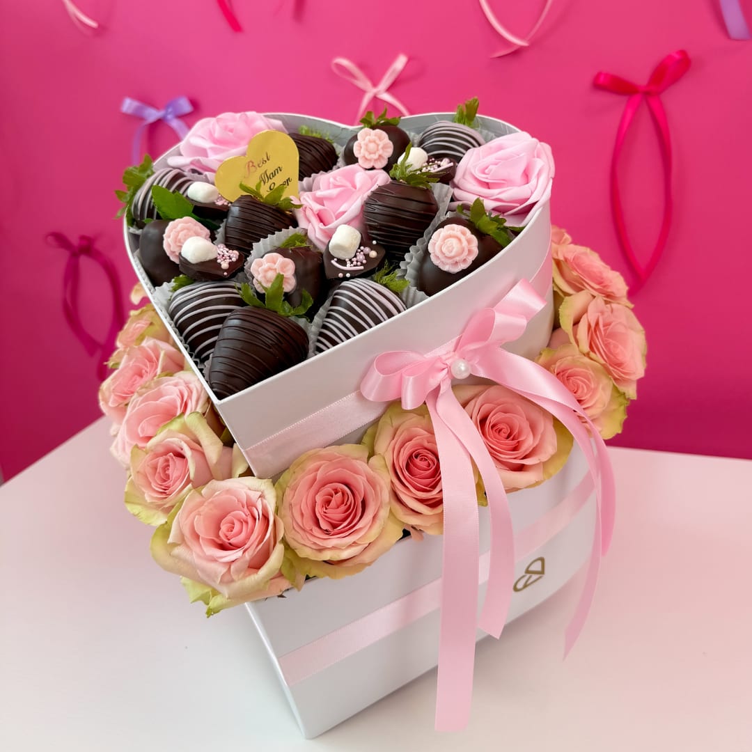 Caja Corazón Deluxe - lowers and Chocolate Gifts Box Surprise your mom with exquisite gifts from Eternal Roses. An unforgettable gift for the most important woman in your life. This elegant heart-shaped box features gourmet chocolate-covered strawberries, detailed with floral decorations, and is surrounded by a stunning ring of fresh pink roses — the perfect mix of sweetness and beauty.  Includes:   Hand-dipped strawberries in dark and white chocolate  Decorated with mini silk flowers and marshmallow details  Surrounded by a full ring of 18 - 22 fresh pink Roses  Finished with a satin pink bow and heart topper with “Best Mom Ever”  Elegant white heart box with double ribbon detail  Guaranteed delivery on Mother’s Day (Sunday, May 12)