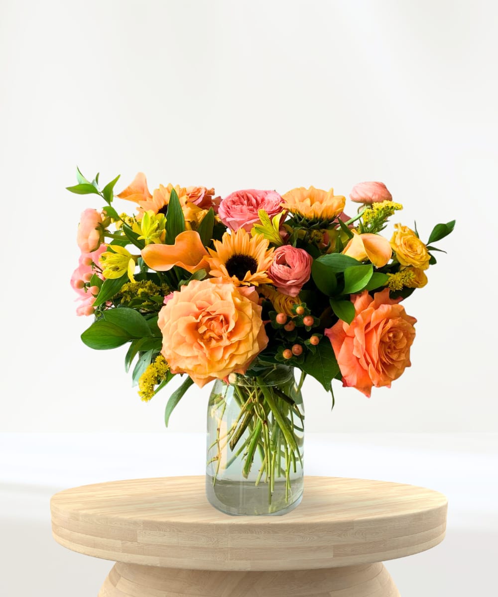 Daybreak Delight Daybreak Delight - Inspired by the rich hues of a sky kissed by sunrise and sunset, the Daybreak Delight is a radiant expression of warmth and joy. Vibrant garden roses, cheerful sunflowers, delicate ranunculus, and sculptural calla lilies are artfully arranged over lush greenery in a classic glass milk jug vase. With layers of color and texture in shades of golden yellow, peach, and orange, this bouquet is the perfect way to say thank you, happy birthday, congratulations, or just because. What’s included: Sunflowers, Garden Roses, Ranunculus, Mini Calla Lilies, and Seasonal Foliage in a Glass Vase.