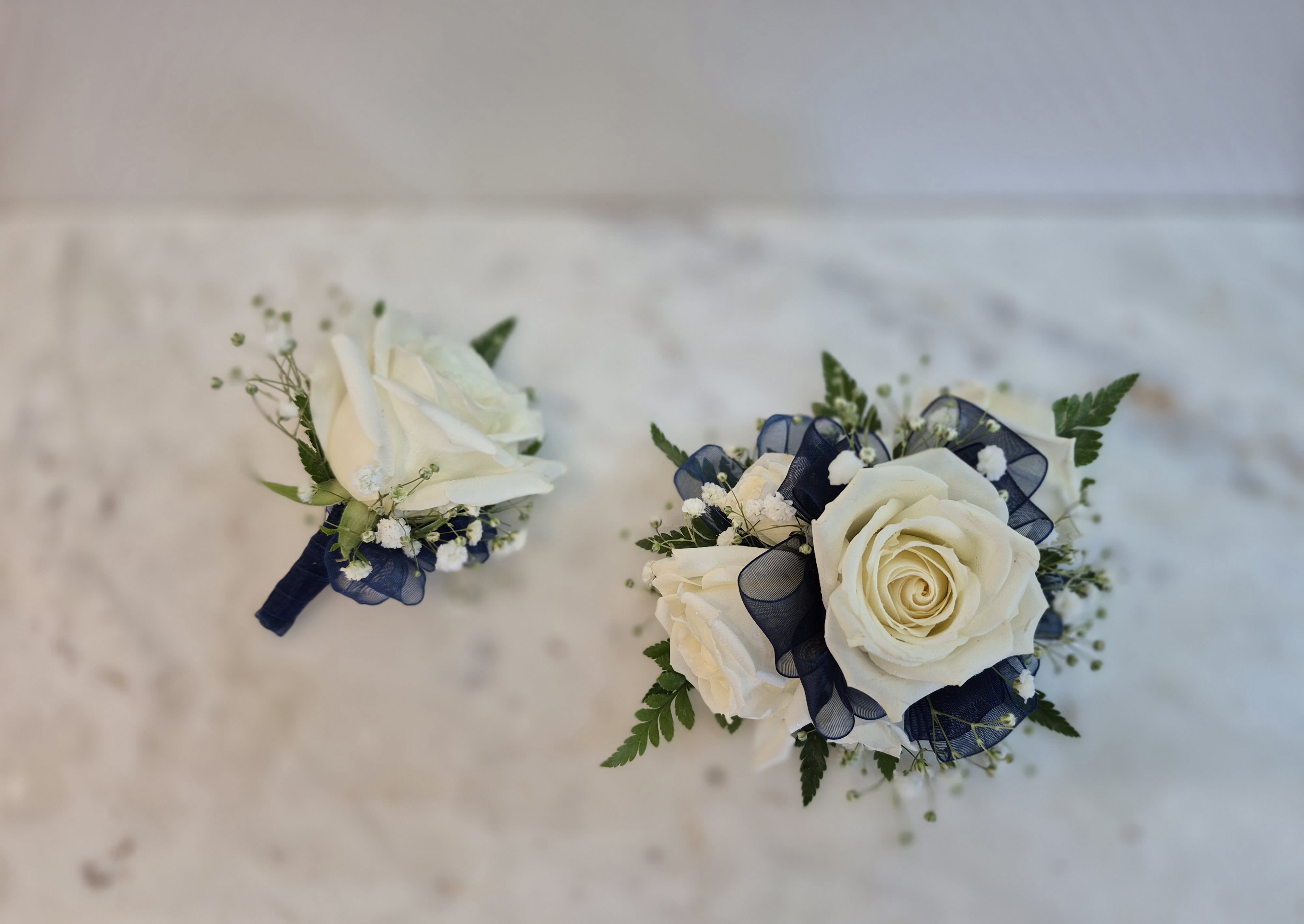 Perfect Prom Corsage &amp; Boutonniere  - Prom flower ideas : beautiful perfect prom white rose wrist corsage, boutonniere and petite handheld bouquet for prom. All designs are completed with a lovely matching purple chiffon ribbon. Order as a set or individually.  Professionally designed perfect prom flowers or wedding flowers. Beautiful wrist corsage for prom and wedding.  Purple prom corsage is 4 inches wide and 4 inches high with 3 roses, white babies breath and 1 jewel and comes with a stretchy elastic wrist band. Upgrade the wristband to a prom corsage bracelet for $10 more: rhinestone or pearl bracelet option  Purple prom bouquet is 6-7 inches across with 9 mini roses, white babies breath and 6 cubic zirconia jewel stems.  Pom boutonniere is 3 inches wide and 3 inches long with 1 rose bud, white babies breath and 1 purple jewel stem. Includes a pearl head pin to attach the mens boutonniere to his suit lapel.