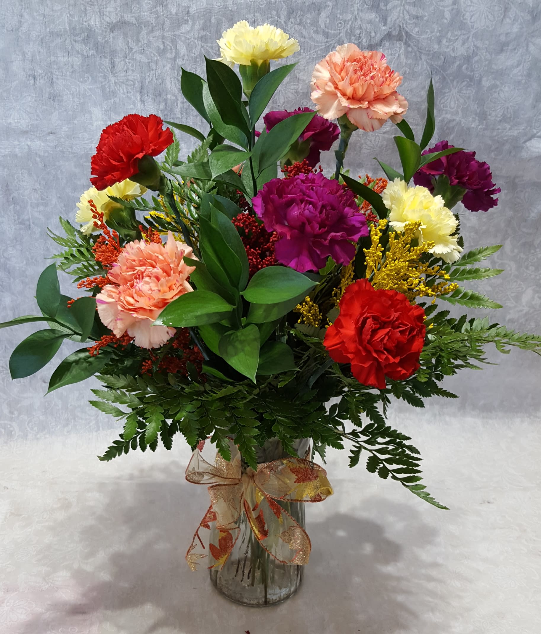 Dozen Fall Colored Carnations Dozen Fall Colored Carnations - Twelve mixed fall color carnations in a vase with filler and greenery. COLORS AND FILLER FLOWERS WILL VARY WITH AVAILABILITY. Deluxe version will have 24 mixed color carnations.