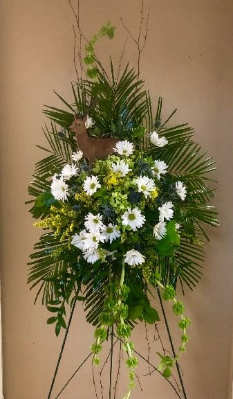 A Hunters’ Remembrance Spray - Looking for a spray in remembrance of an avid outdoorsman or woman. This spray pays tribute to their memory. With the look of a field full of wildflowers, highlighted with a deer standing watch... made up of mixed greens, wood, daisies, bells of Ireland, and yellow wildflowers.