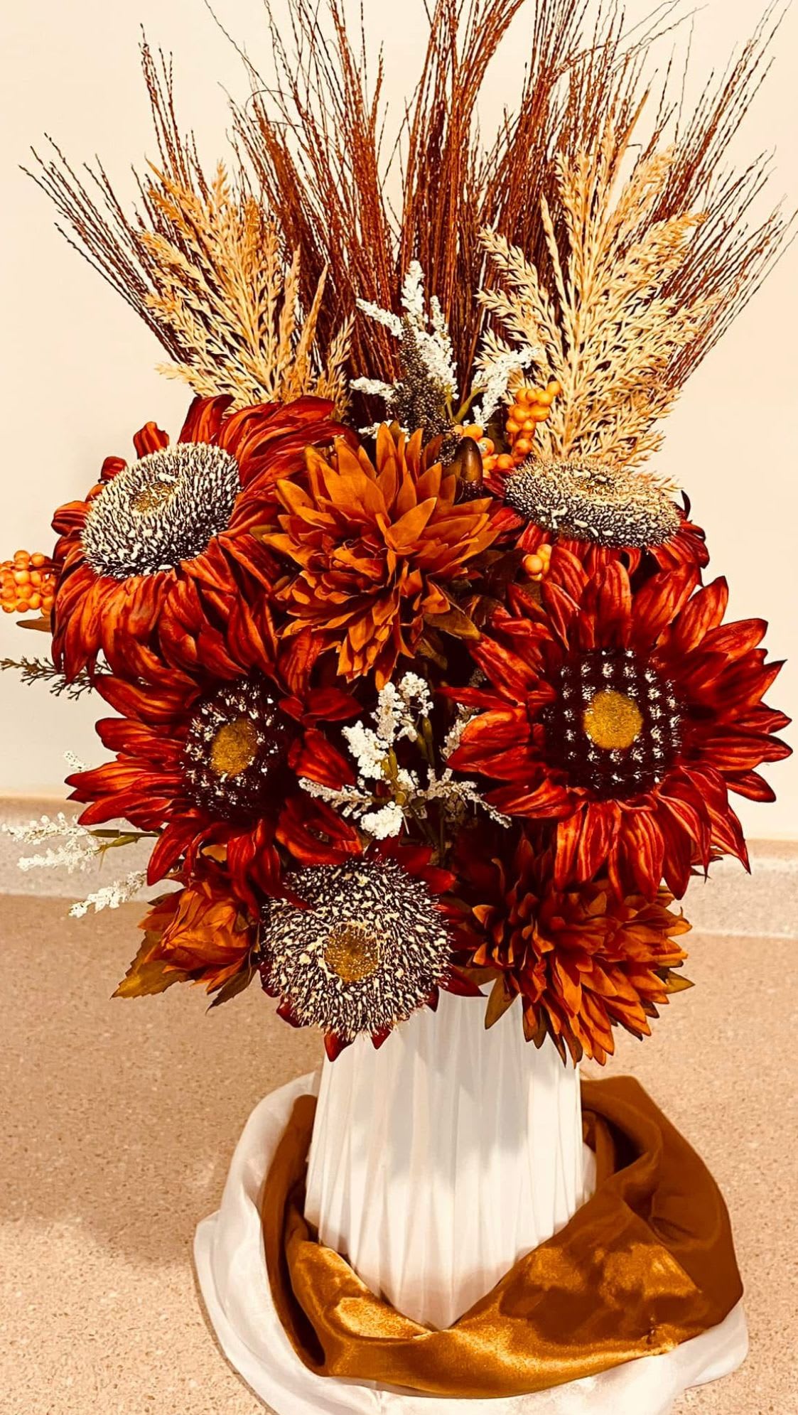 Forever Autumn By Shelly - Capture the beauty of fall all year long with this handcrafted silk arrangement. Bursting with rich seasonal tones, textured grasses, and bold blooms, it’s styled in a striking white vase with warm golden detailing. Designed to be enjoyed season after season, this piece brings lasting elegance to any space.  Perfect for entryways, dining tables, or as a thoughtful gift that never fades.