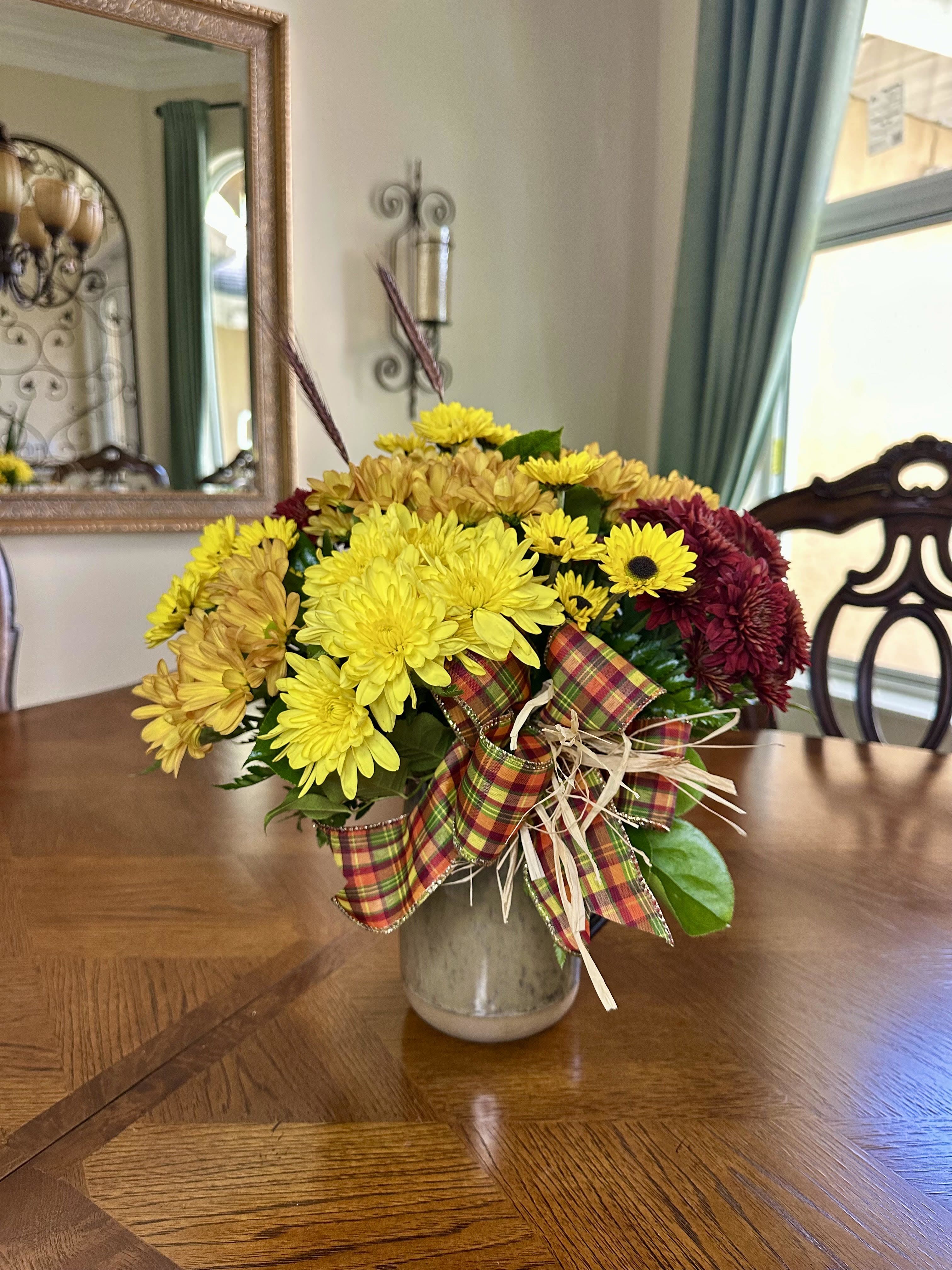 Autumn Charm Bouquet Autumn Charm Bouquet - Bring the warmth of the season into your home with our Autumn Charm Bouquet. Bursting with golden yellow, rustic orange, and deep burgundy mums, this charming arrangement captures the heart of fall. Accented with a festive plaid bow and natural raffia, it’s artfully arranged in a rustic ceramic vase—perfect for a cozy centerpiece or thoughtful gift. Celebrate the beauty of autumn with a bouquet that radiates cheer, comfort, and seasonal charm.