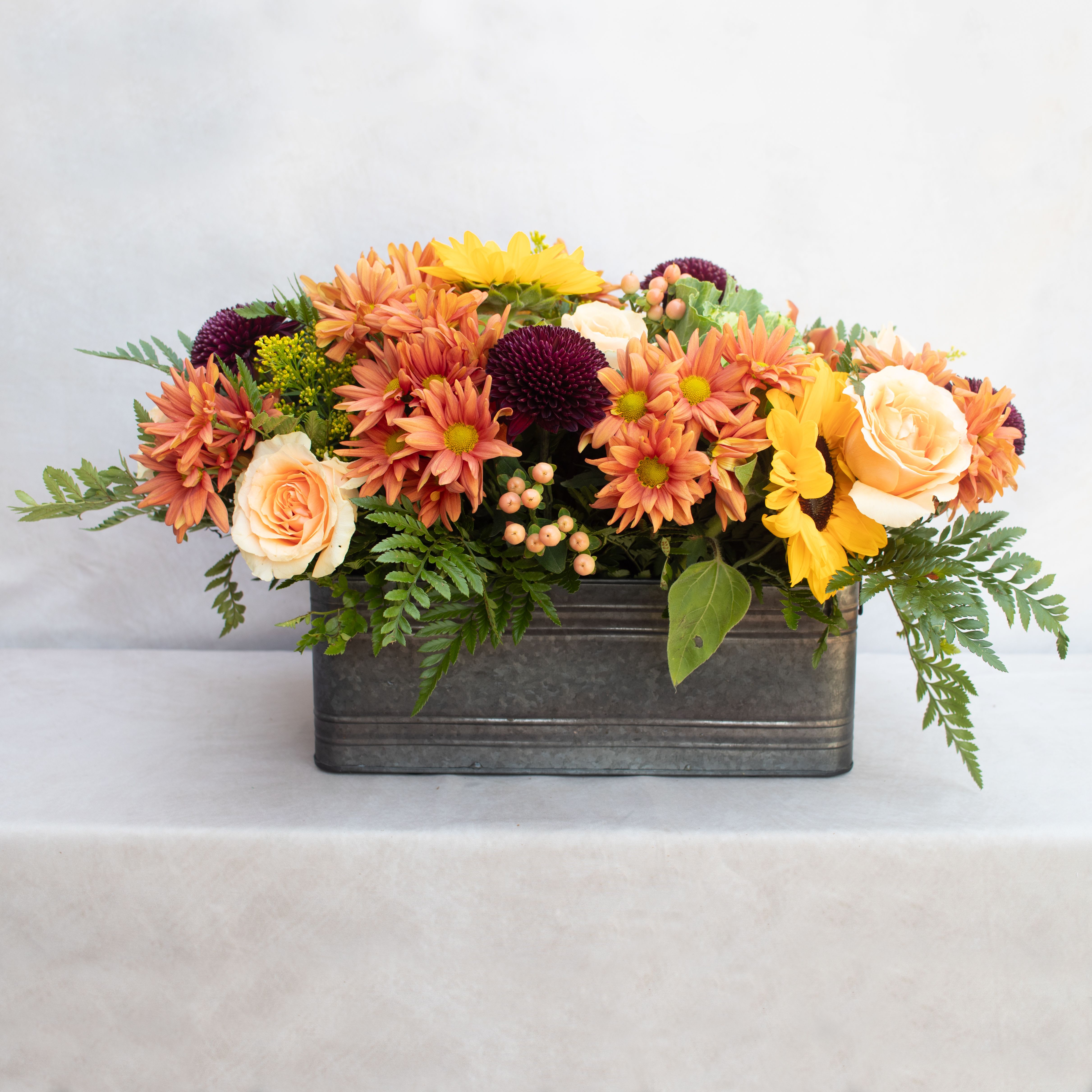 VINTAGE SEASONAL CENTERPIECE  - FALL CENTERPIECE DESIGNED LONG AND LOW WITH SEASONAL FLOWERS LIKE DAISIES, CREMONS, ROSES, SUNFLOWERS, BERRIES AND A MIXTURE OF GREENERY FOR TEXTURE. ARRANGEMENT IS ABOUT 16LX9H. PERFECT ADDITION TO A LONG TABLESCAPE. 