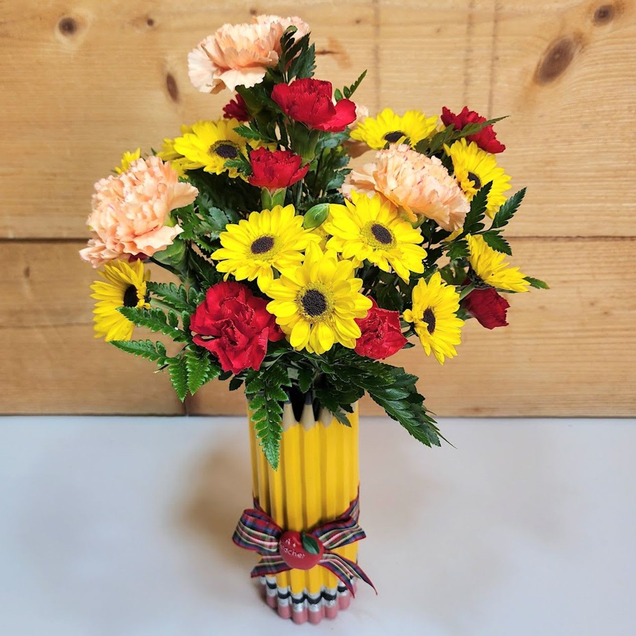 Bright Start Blooms - Celebrate the excitement of a new school year with our Bright Start Blooms! This cheerful back-to-school arrangement features sunny yellow daisies, vibrant red carnations, and soft peach carnations, all accented with fresh greenery. Presented in a playful pencil-themed container and tied with a colorful bow, it’s the perfect gift to show appreciation for teachers, encourage students, or add a touch of classroom joy. A fresh and thoughtful way to start the school year on a bright note!  Approx 16&quot; H x 8&quot; W     PLEASE NOTE: Some flowers, vases and other products pictured are subject to availability, and may be substituted for a similar item if unavailable according to our substitution policy.