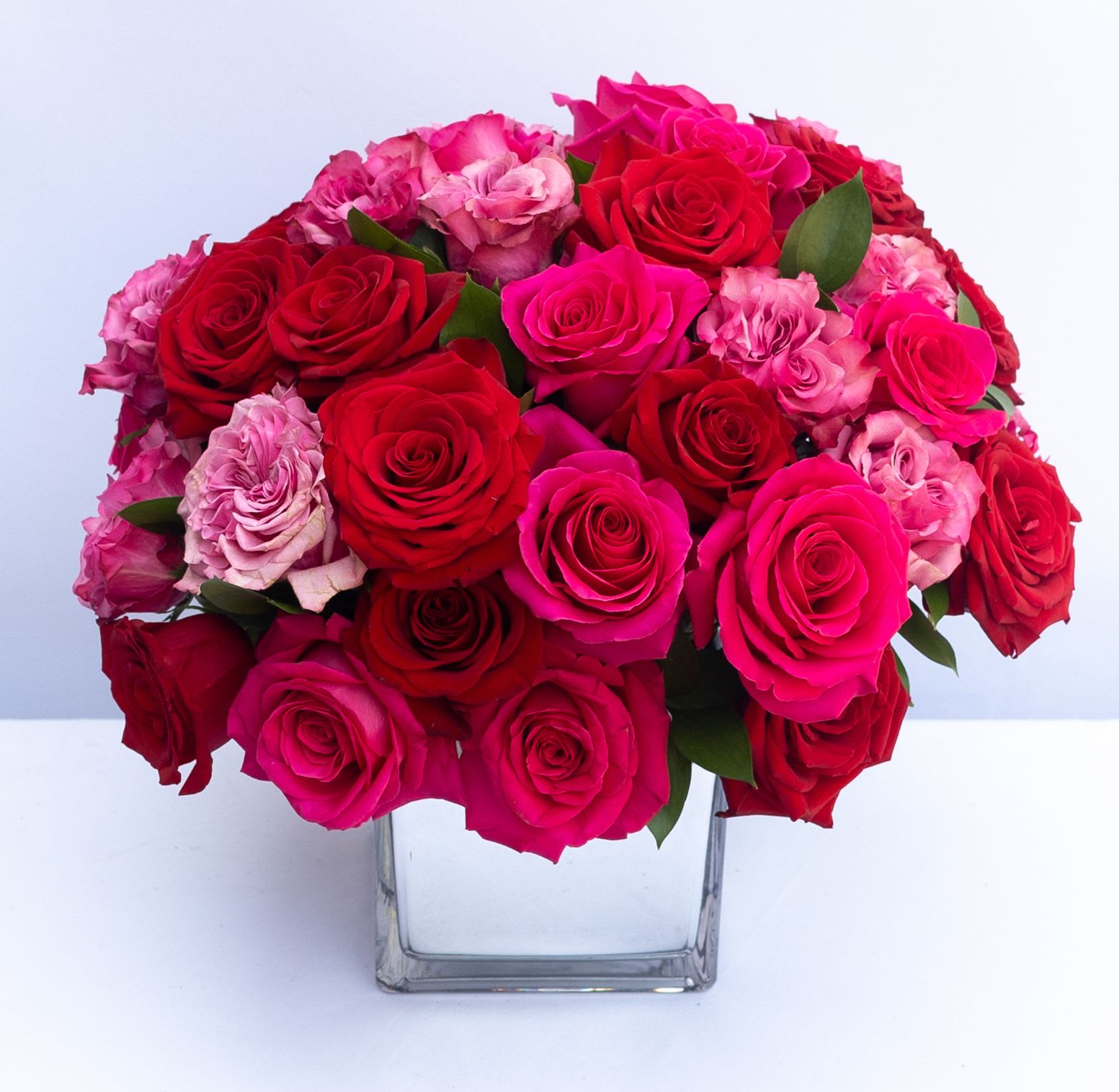 The Blushing Extravagance Luxury Bouquet - Designed to capture the heart this bouquet goes above and beyond to create a space where modern style and love’s every wish unite. Hot pink roses red roses and red spray roses are arranged to perfection and embellished with sparkling stone accents at the center of select blooms as well as silver wires to create a fascinating looping effect taking the average rose bouquet to a new level of sophistication. Tying everything together is the modern mirrored vase that brings light and love to this unique design.