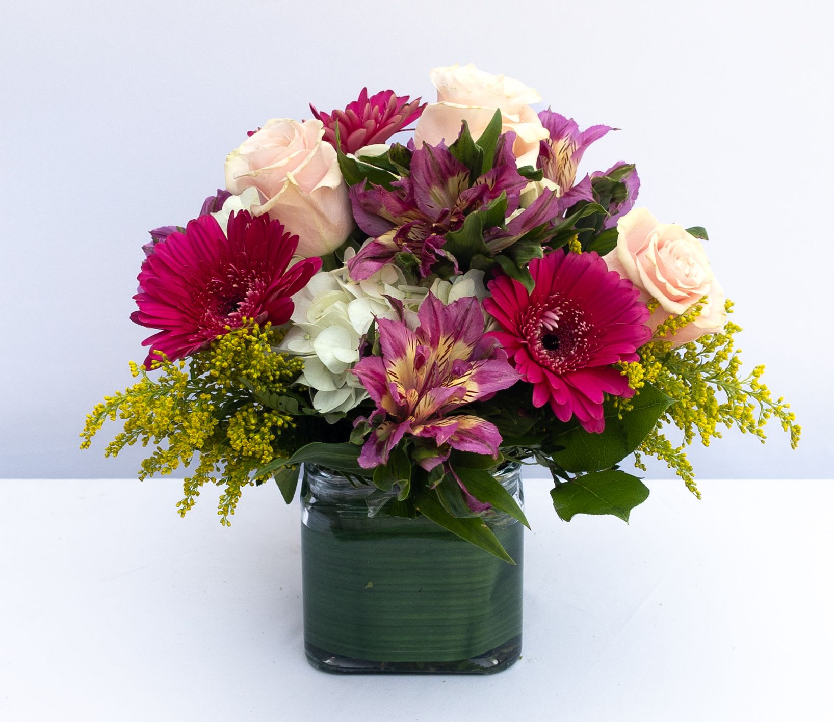 Spring Garden Spring Garden - Mixed flowers arranged in a modern mounded design in assorted spring colors. Gerberas, alstroemeria, hydrangeas, roses, and other seasonal flowers. 5x5 clear cube with leave wrapped inside. The arrangement is about 12hx12w.
