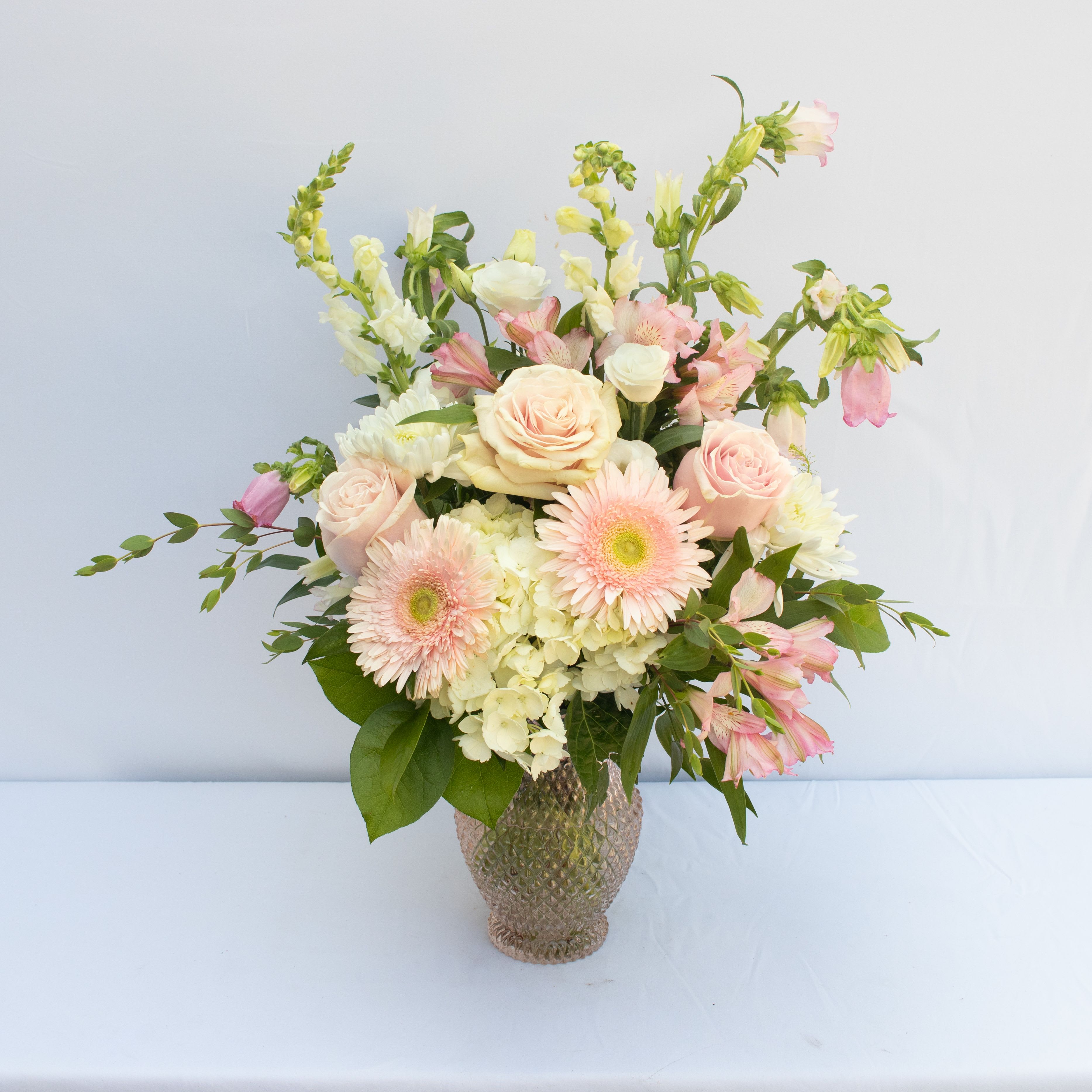 PINK SKY PINK SKY - A SOFT MITXTURE OF WHITE AND PINKS TO INCLUDE SOME OF THESE FLOWERS SNAPDRAGONS, HYDRANGEA, ROSES, GERBERAS, LISIANTHUS, RANUNCULUS, CAMPANULA, ALSTROMERIA, MUMS ACCENTED WITH GREEN DRAGON ARRANGEMENT MADE IS ABOUT 14HX8W. ARRANGEMENT IS IN A SOFT PINK BUBBLE TEXTURED VASE.
