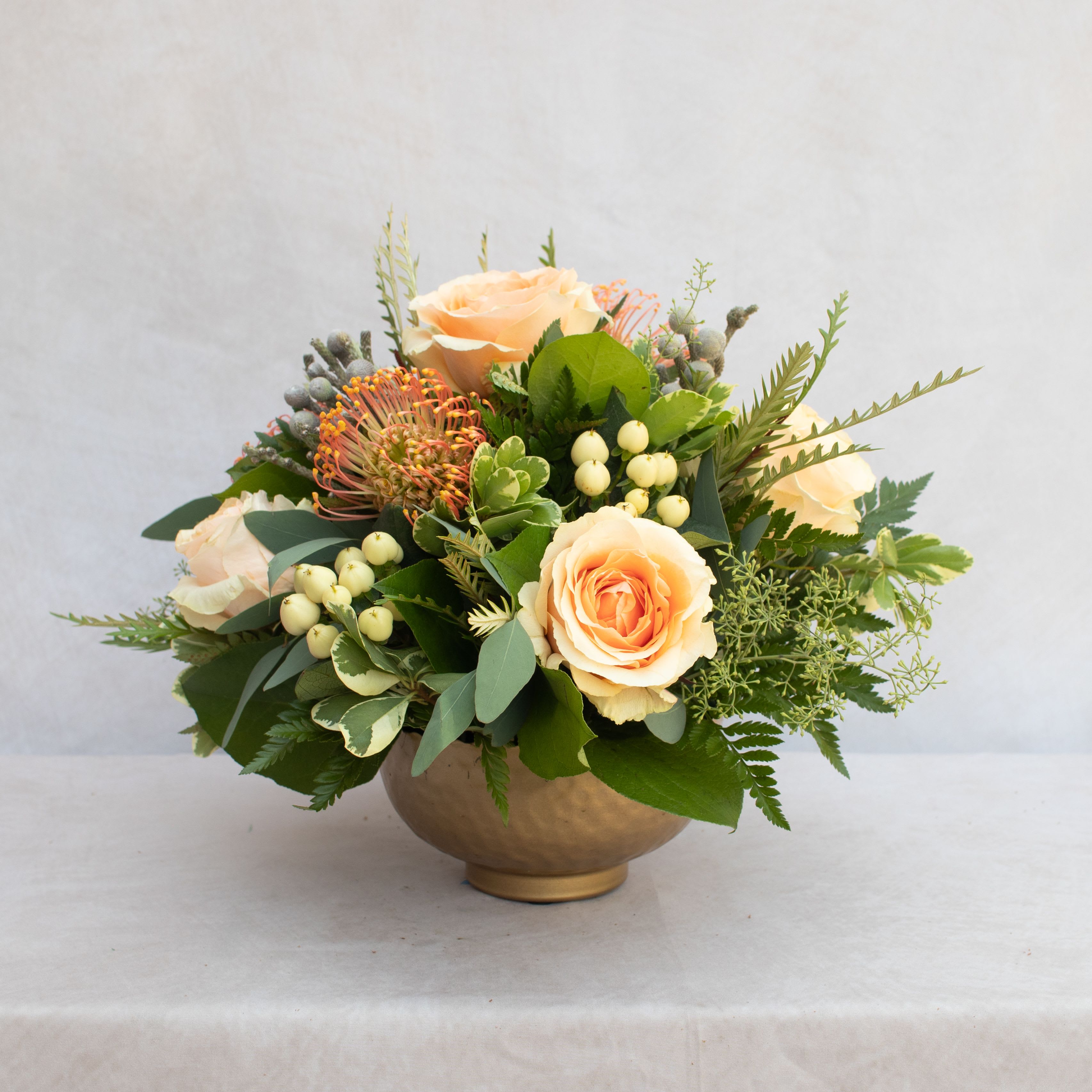 PEACHES &amp; CREAM  - Peach roses, Proteas, berries, mixed with a variety of greenery in a gold compote. The arrangement is about 12x12.  Golden Compote is 4Hx5W