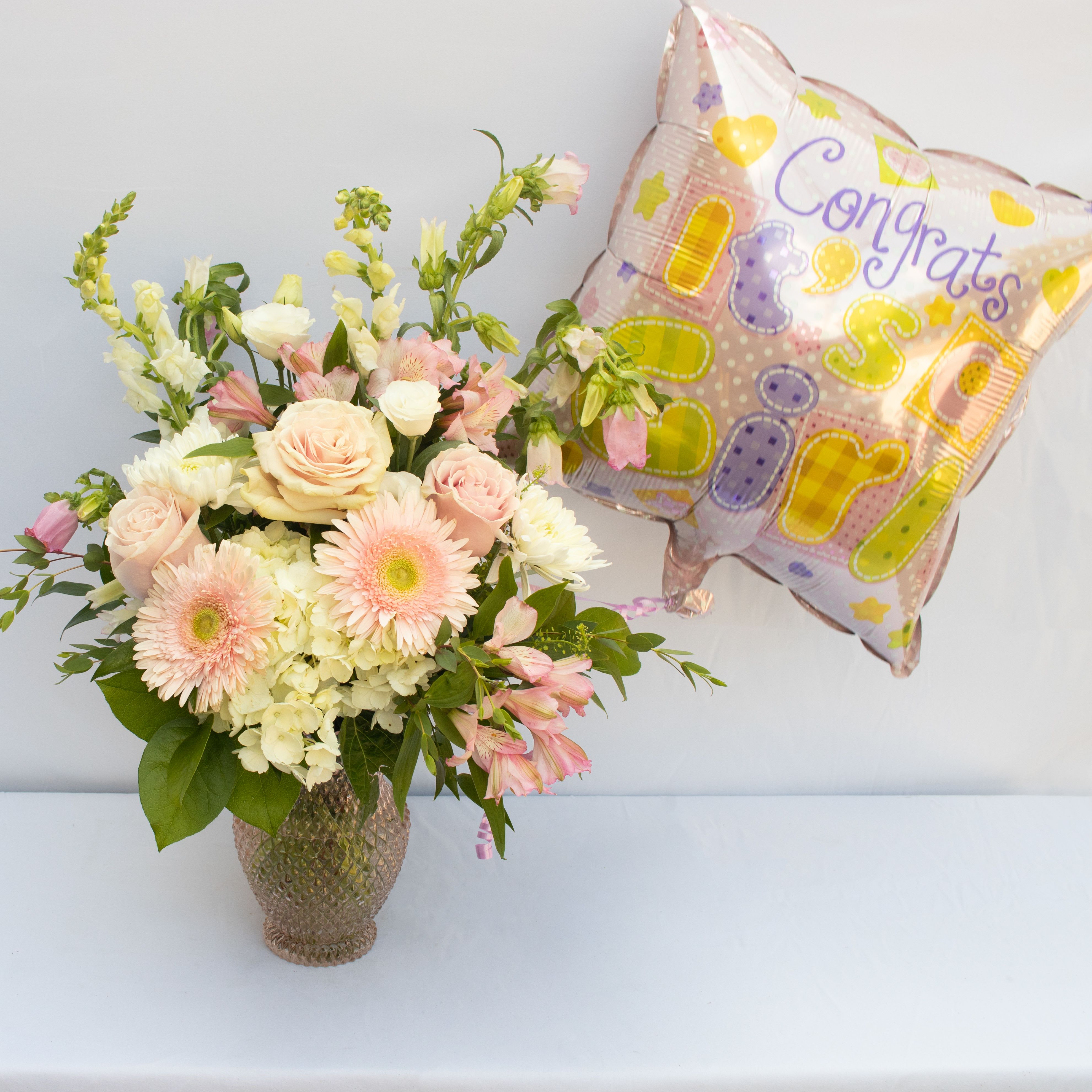 IT'S A GIRL!  - PINK SKY ARRANGEMENT WITH AN &quot;IT'S A GIRL&quot; BALLOON, A SOFT MIXTURE OF WHITE AND PINKS TO INCLUDE SOME OF THESE FLOWERS SNAPDRAGONS, HYDRANGEA, ROSES, GERBERAS, LISIANTHUS, RANUNCULUS, CAMPANULA, ALSTROMERIA, MUMS ACCENTED WITH GREEN DRAGON ARRANGEMENT MADE IS ABOUT 14HX8W. ARRANGEMENT IS IN A SOFT PINK BUBBLE TEXTURED VASE. 