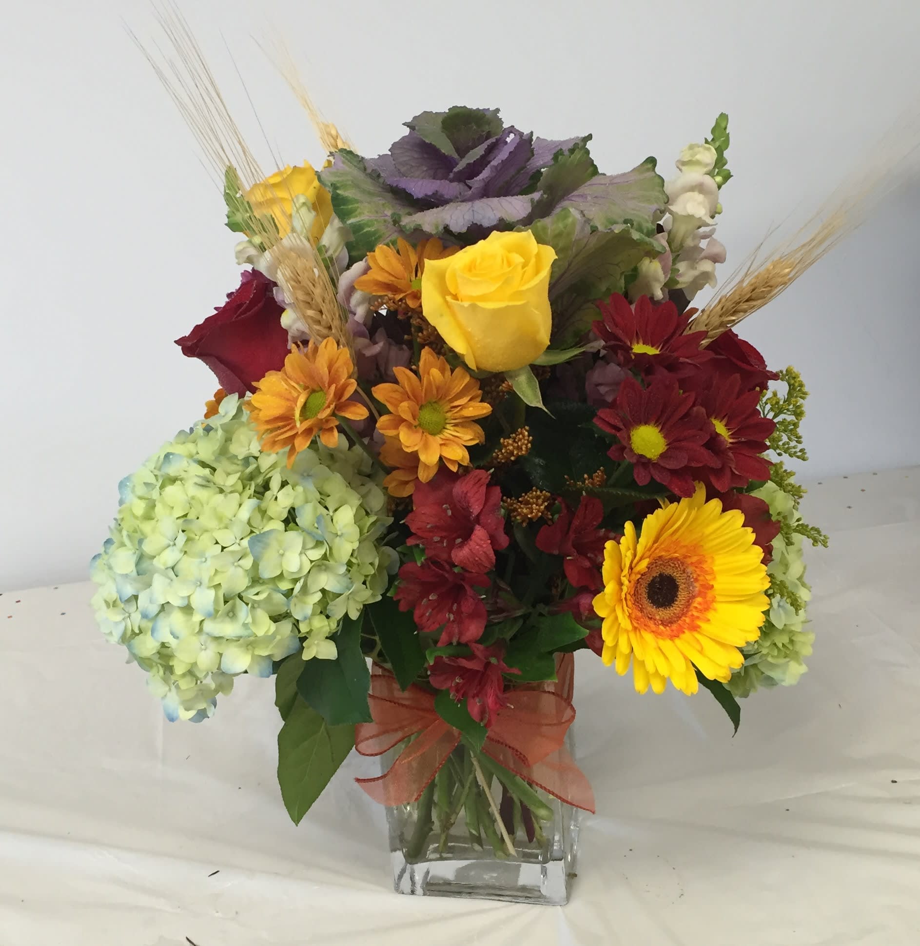 Autumn Wheat Whispers Autumn Wheat Whispers - Blue Hydrangea, Daisies, Gerbera daisies and Alstroemeria express the beauty of fall foliage for fall holidays, a friendship or just to show that you care in a rectangle clear glass vase.