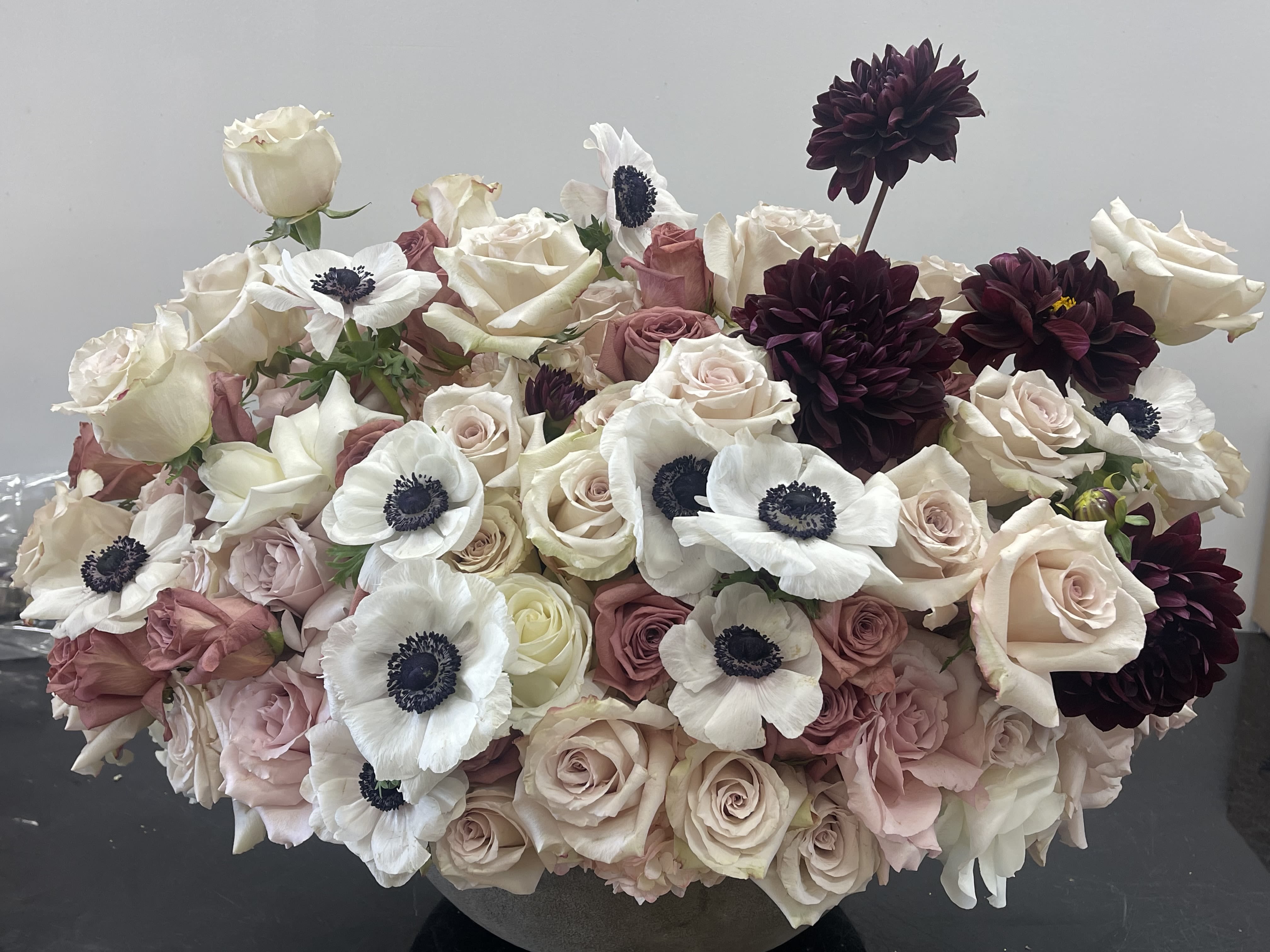 Dusky Romance - A lush and romantic arrangement designed with layered roses in soft ivory, blush, and dusty pink tones, accented with delicate white anemones and rich burgundy dahlias for contrast. The composition is full, rounded, and elegant—perfect for all occasions. events, or as a statement centerpiece   Some florals are seasonal, if particular flower will not be available due to season, we will substitute for similar flower, composition, color pallet and value of the arrangements as closely as possible. All effort to create a floral arrangement as close to the photo shown, the actual arrangement may vary slightly in its appearance from the photo shown. If you have any questions about your order, we welcome you to call us or email 