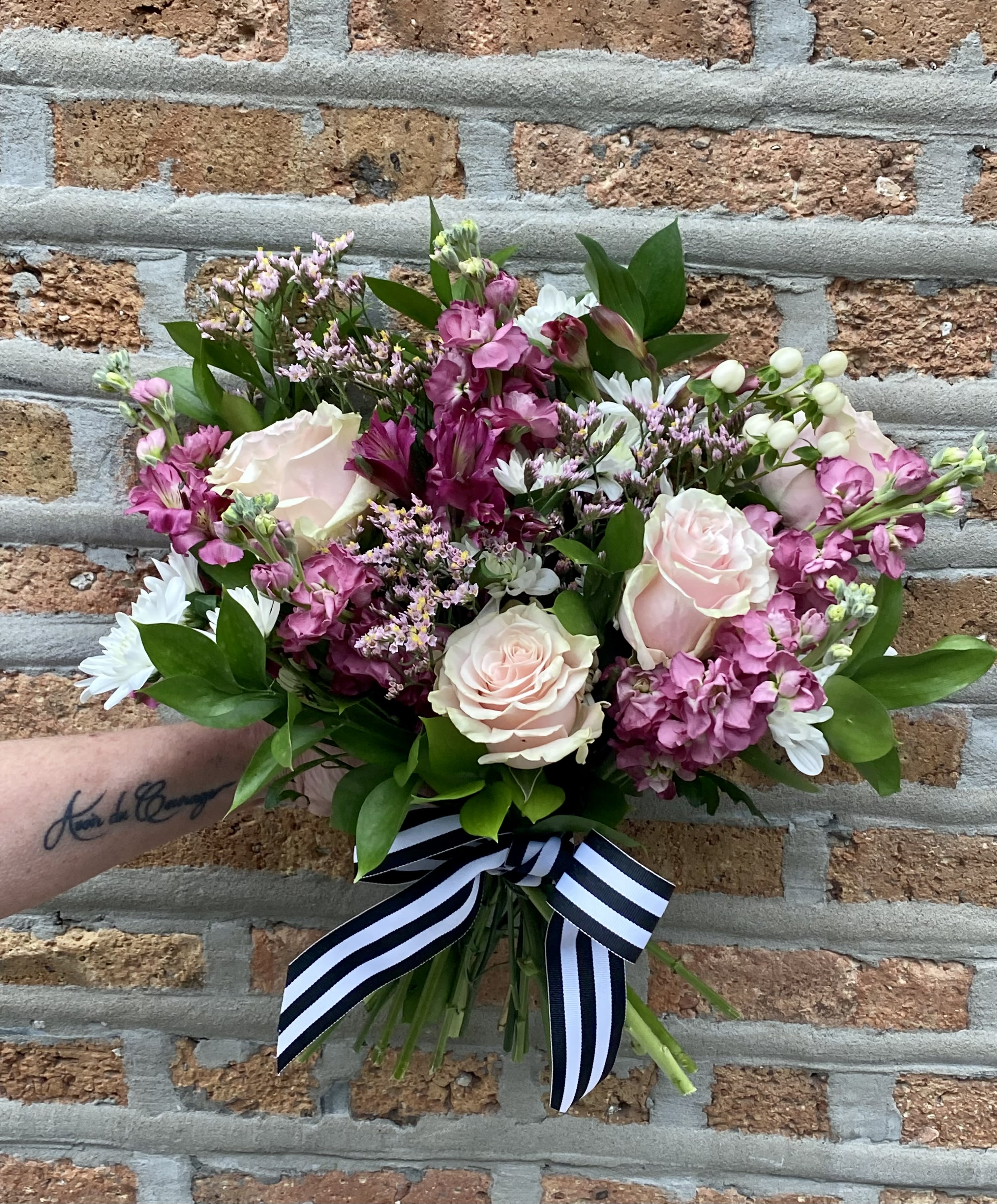ENCHANTED Hand Tie or Vase Bouquet ENCHANTED Hand Tie or Vase Bouquet - Specialty Pink Roses, Mauve stock, purple alstromeria, accent florals and greens in a wildflower style bouquet.