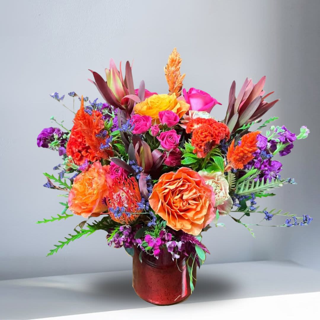 Innerbloom - Recipe: Orange Roses, Hot Pink Roses, Spray Roses, Purple Stock, Celosia, Amarath, Pincushion protea, Pink Carnations, Conebrush Safari, Sweetwilliam, and Greens in a round, red vase. Availability: Celosia late spring-fall	 Design View: All Facing View Photo shown: Standard 