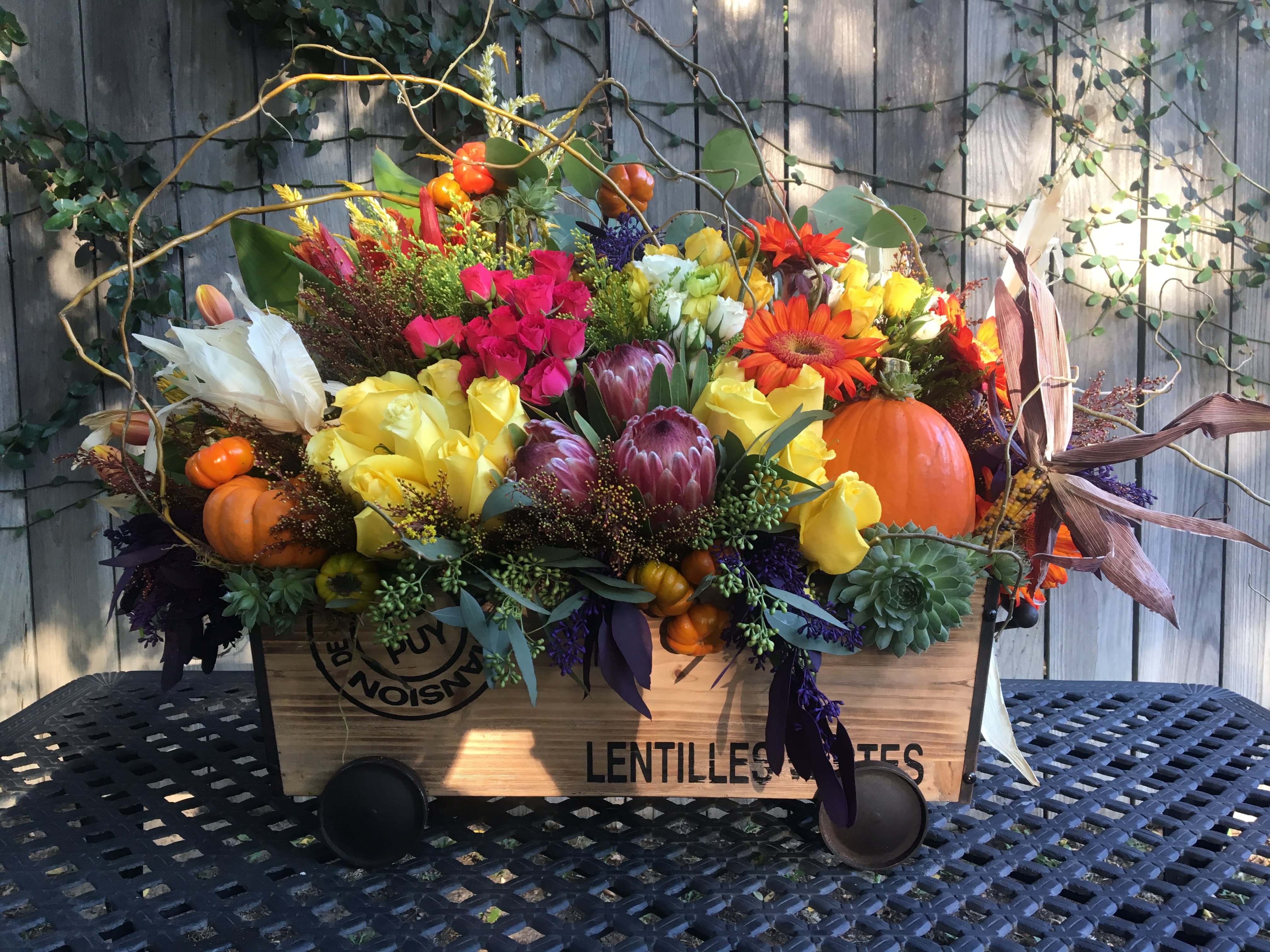 Benvenuto autunno Benvenuto autunno - The best season has finally arrived- welcome autumn! This lovely arrangement features vibrant fall colors- burnt orange, gold, amber, the colors of the season. You will find a mixture of yellow and pink roses, tulips, succulents, mini pumpkins, corn, and other special touches all inside of a rustic wooden wagon. The perfect touch to say hello to fall.