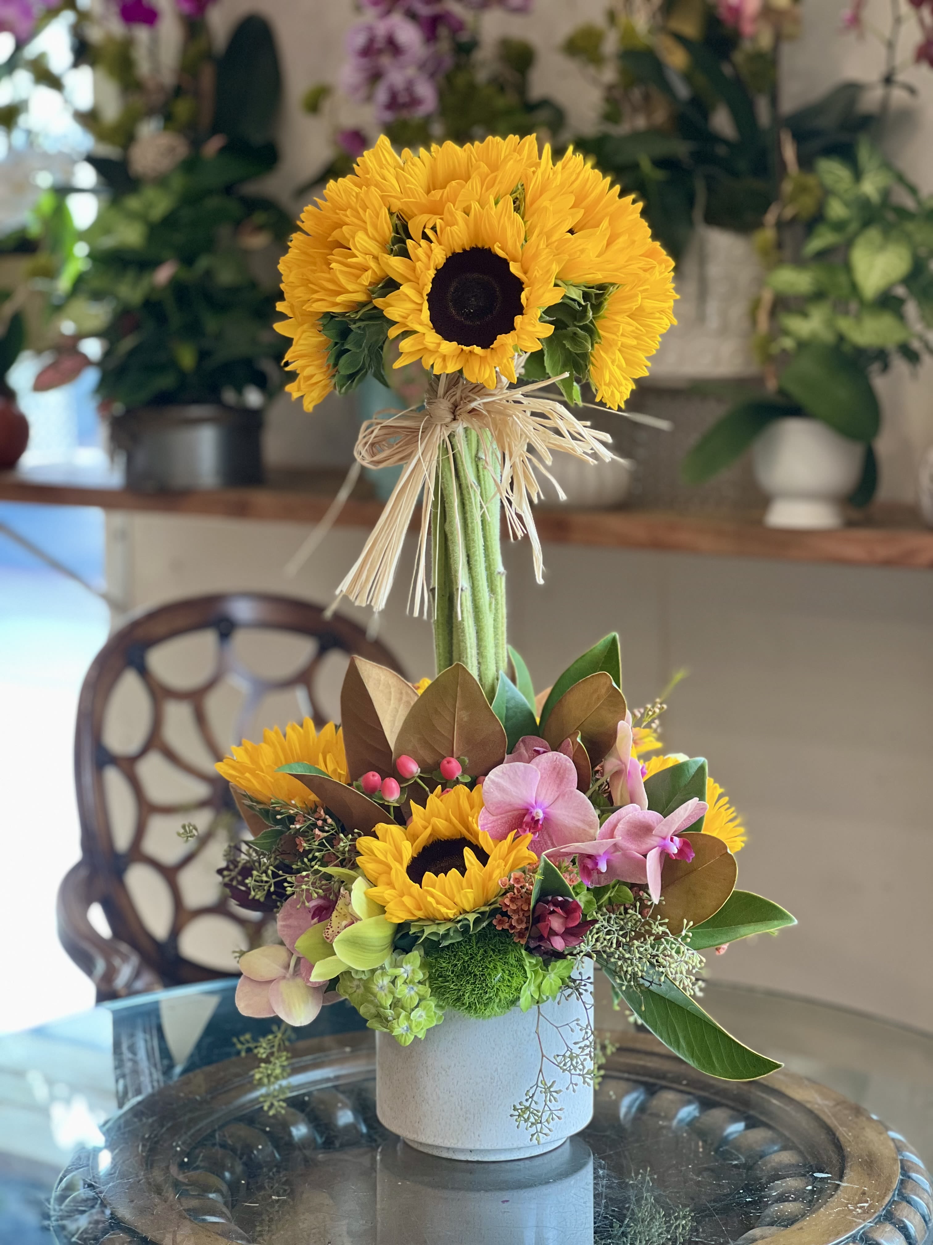Sunflower Topiary  Sunflower Topiary  - Flowers: 12 sunflowers wrapped together and base flowers such as green hydrangeas, sunflowers, green cymbidium, orange orchids, hypericum berries, dianthus, and greenery.   Vase: 6x6 white ceramic