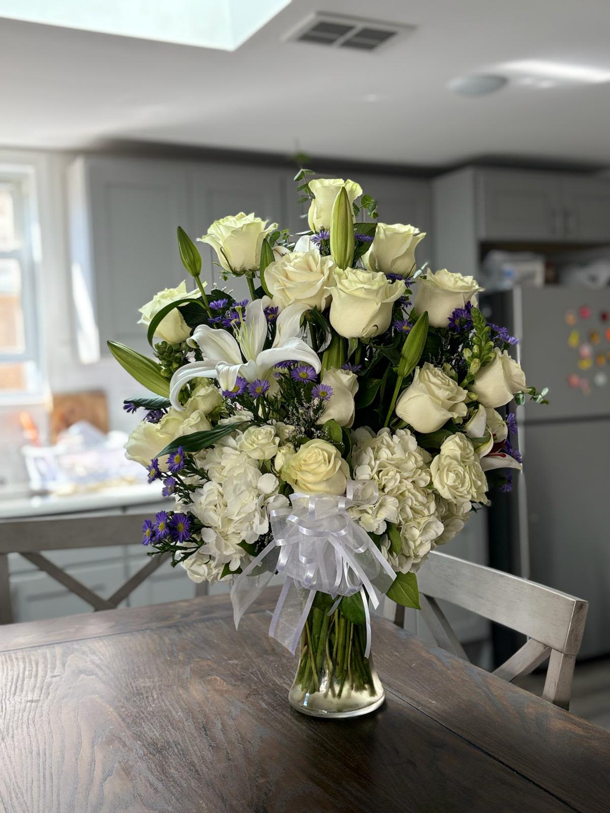 Timeless Elegance -  Elegant Design  A classic arrangement that exudes sophistication and grace. This setup features fresh white roses, lilies, and delicate blooms. Accented with soft greenery, it adds a perfect touch for any elegant space or meaningful occasion. The combination of flowers and greenery creates a harmonious and refined look.  Key Features Fresh White Roses: Adds a delicate and elegant touch. Lilies: Enhances the arrangement with a classic and graceful presence. Delicate Blooms: Provides a soft and refined appearance. Soft Greenery: Adds a natural and soothing element to the arrangement. Perfect for Elegant Spaces: Ideal for adding a touch of sophistication. Meaningful Occasions: Suitable for special events and celebrations.