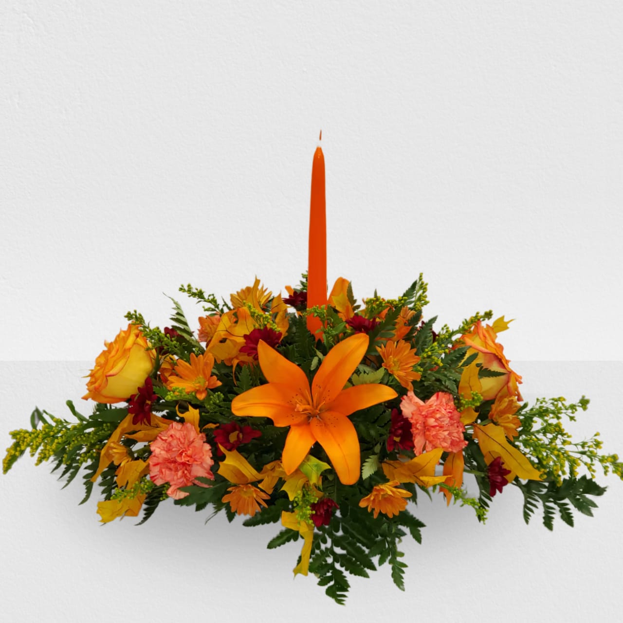 Classic Fall Centerpiece -  Standard 1 candle, 2 orange roses, 2 orange lilies, 4 orange carnations, burgundy and orange fall daysis,2 solidagos and fall leaf.  Deluxe: 2 candles, 4 orange roses, 4 orange lilies, 4 orange carnations, burgundy and orange fall daysis, 3 solidagos and fall leaf.  Premium: 3 candles, 6 orange roses,4 orange lilies, 8 orange carnations, burgundy and orange fall daysis, 4 solidagos and fall leaf.