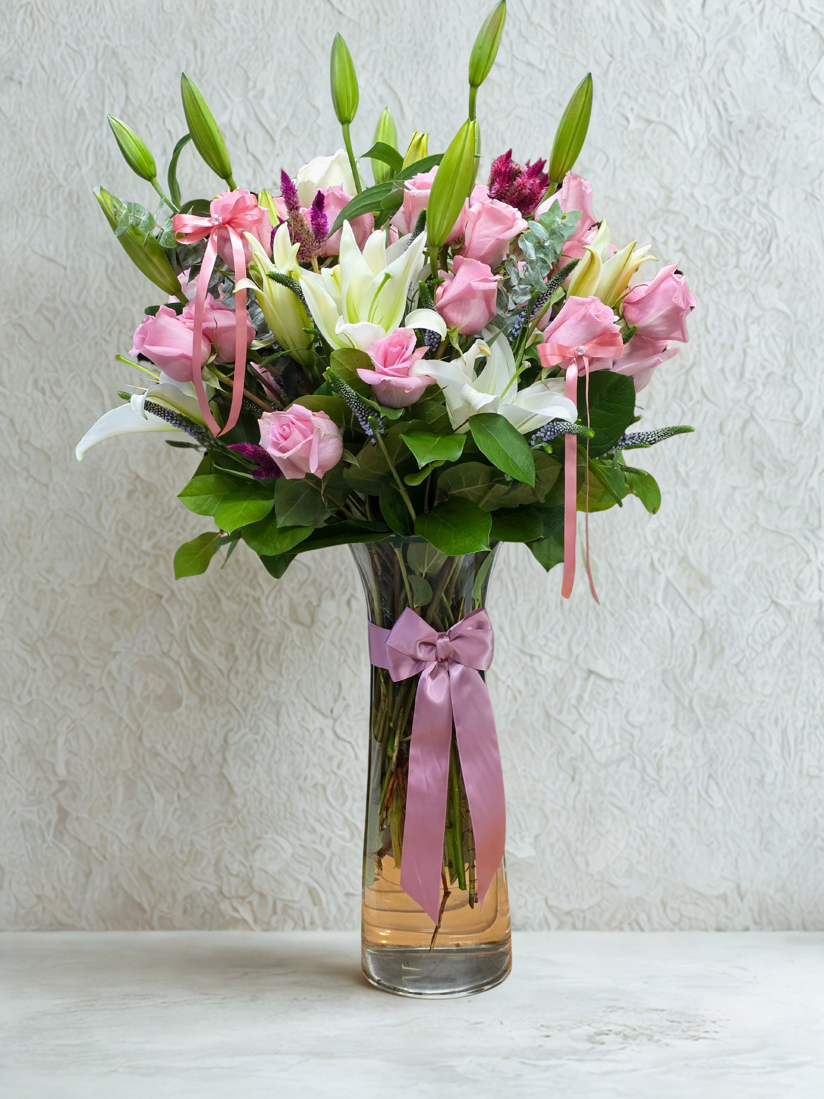 blushing elegance blushing elegance - Soft, romantic, and gracefully timeless — the Blushing Elegance arrangement features a luxurious blend of pink roses, white lilies, and touches of magenta celosia, surrounded by lush eucalyptus greenery. Presented in a tall glass vase with a satin pink ribbon, this piece radiates sophistication and charm. Perfect for anniversaries, birthdays, or simply to express love and admiration, this bouquet brings a gentle glow to any room. Each flower is carefully selected for freshness, fragrance, and beauty — creating an arrangement that feels as heartfelt as it looks.