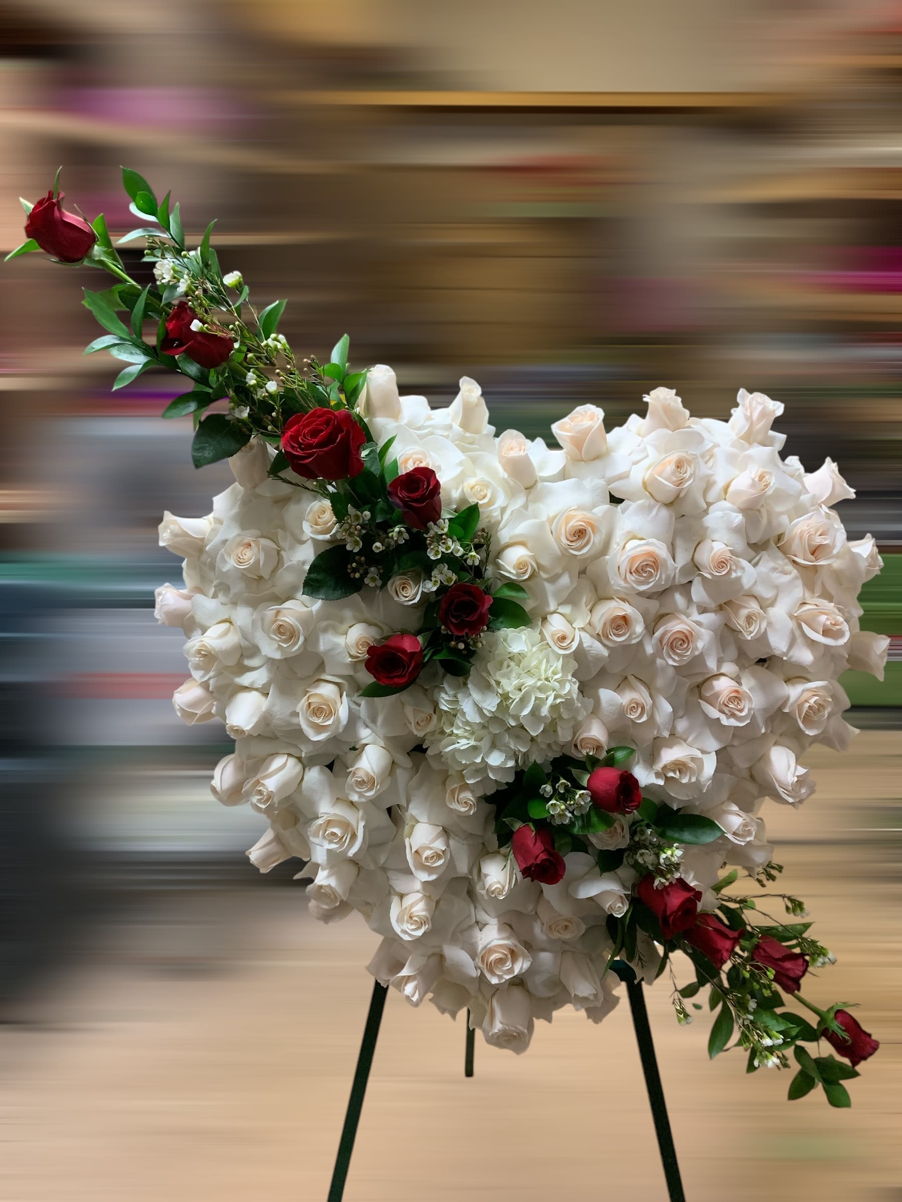 Radiant Rest - This elegant heart-shaped floral arrangement is a powerful expression of love, honor, and remembrance. The base is composed of pristine white roses, symbolizing purity, innocence, and eternal love. Accentuating the design, a cascade of bold red roses flows gracefully along the heart, representing deep affection and admiration. Touches of baby’s breath and lush greenery add texture and softness to the arrangement. Perfectly balanced and exquisitely crafted, this heartfelt tribute radiates grace and beauty, making it a meaningful way to honor and cherish the memory of a loved one.