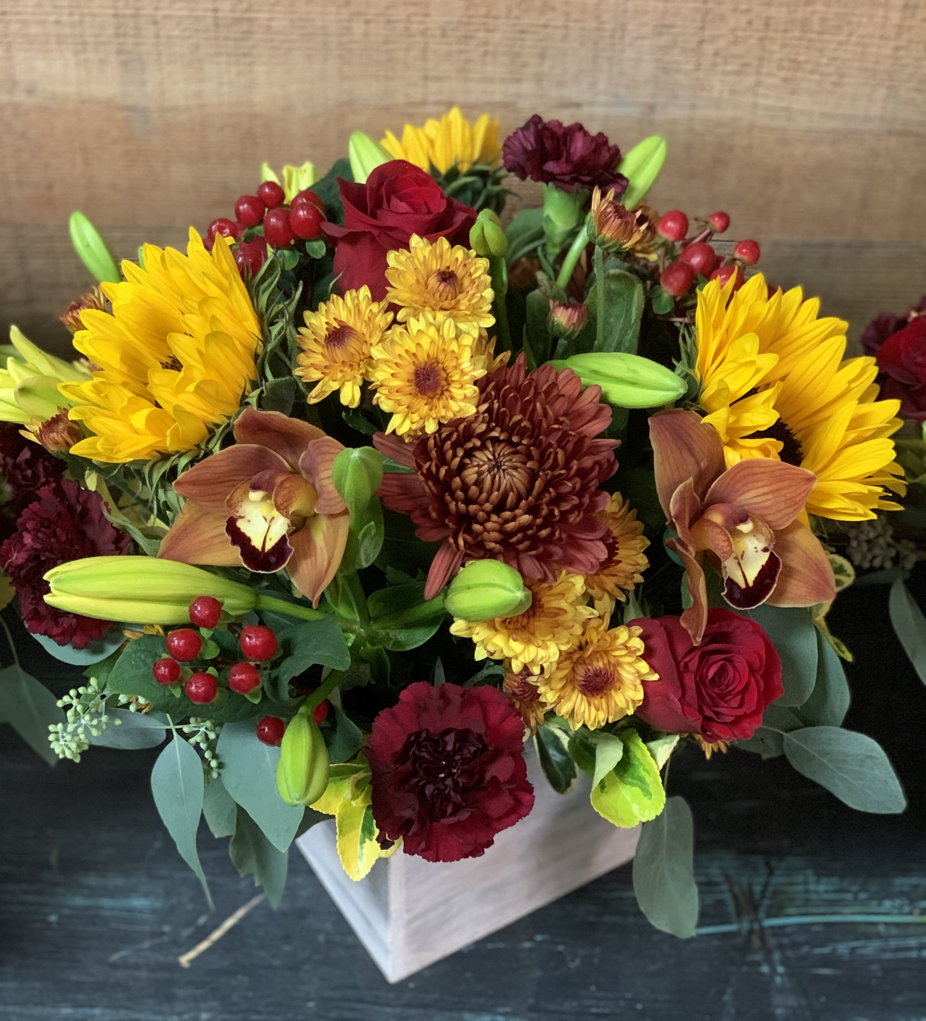 Rustic Autumn - A beautiful arrangement of sunflowers, red roses, burgundy carnations, yellow lilies, and other flowers in a rustic wood cube.  Perfect as a centerpiece for a small family gathering.  Different sizes are for different quantities. Regular- 1 arrangement Deluxe- 2 arrangements Premium- 3 arrangements