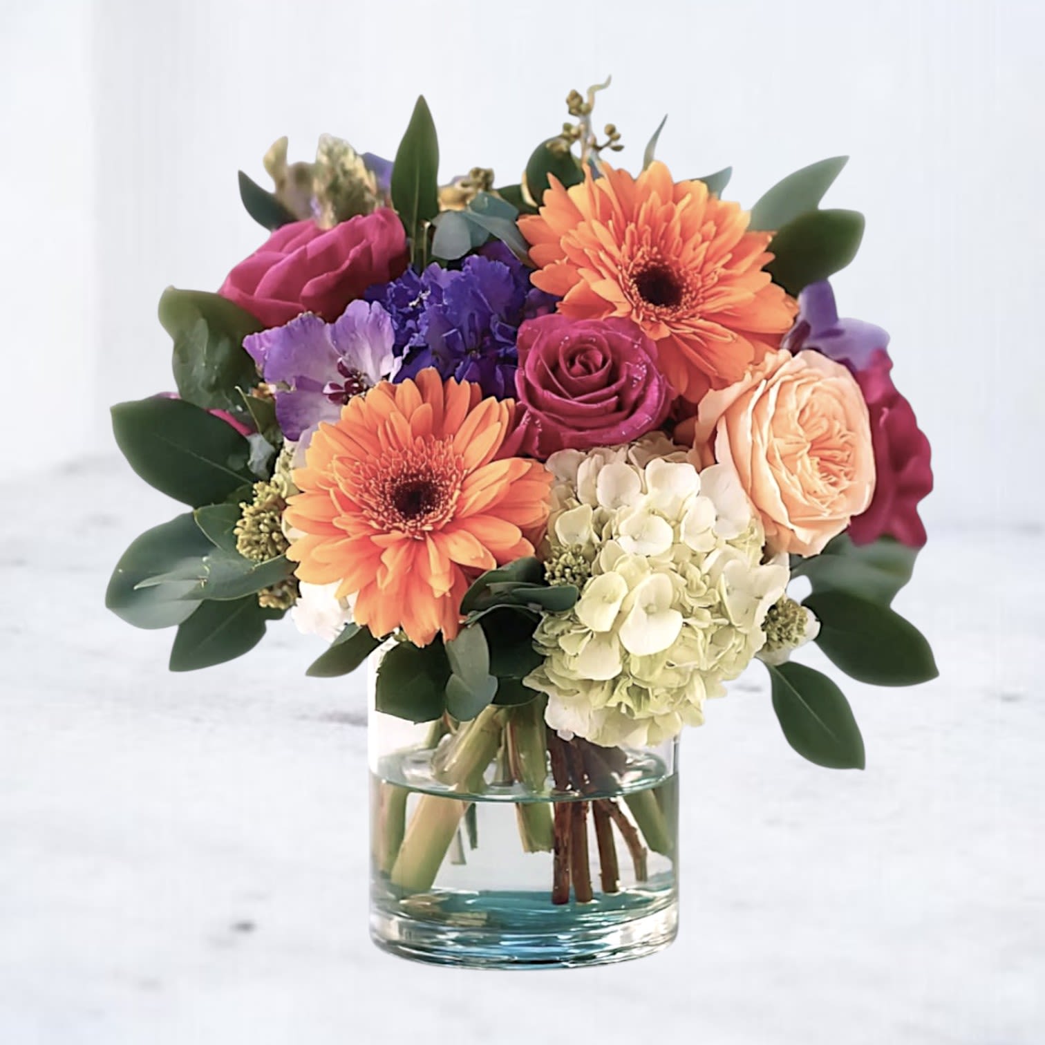 Jubilee Bouquet Jubilee Bouquet - Bring a burst of joy and energy into any space with our Jubilee Bouquet, a lively mix of bold orange gerbera daisies, radiant roses, striking purple blooms, and soft green hydrangea. Perfect for birthdays, celebrations, or simply to brighten someone’s day, this modern arrangement captures the essence of happiness and connection. Hand-crafted by our local florists in Magnolia, The Woodlands, Spring, and surrounding Houston areas, this bouquet is designed for same-day flower delivery. Whether you’re sending birthday cheer, congratulations, or a “just because” surprise, the Jubilee Bouquet is sure to make a lasting impression.