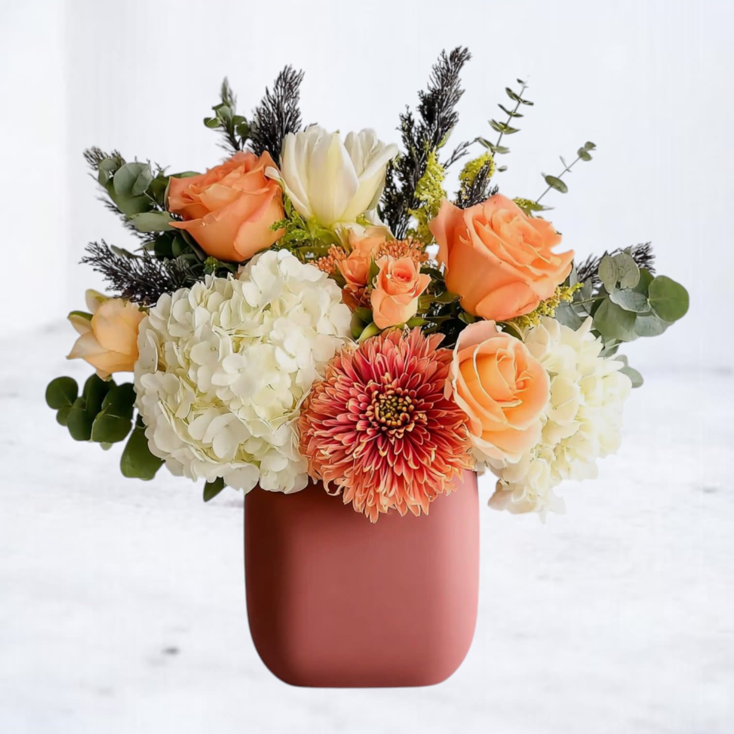 Terra Sunset Terra Sunset - Capture the timeless beauty of fall with our Terra Sunset, a lush arrangement that blends warm peach roses, ivory hydrangea, and a statement chrysanthemum in rich sepia-inspired tones. Nestled in a sleek matte vase, this bouquet radiates cozy sophistication—perfect for celebrating birthdays, expressing gratitude, or simply brightening someone’s day. The soft interplay of peach, cream, and rust-colored blooms creates a vintage warmth reminiscent of a sepia photograph, making this arrangement an elegant choice for both everyday moments and special occasions. Perfect for: Birthdays, Thank You, Fall Flowers, Everyday Gifting Featured blooms: Roses, hydrangea, chrysanthemum, seasonal accents, and eucalyptus