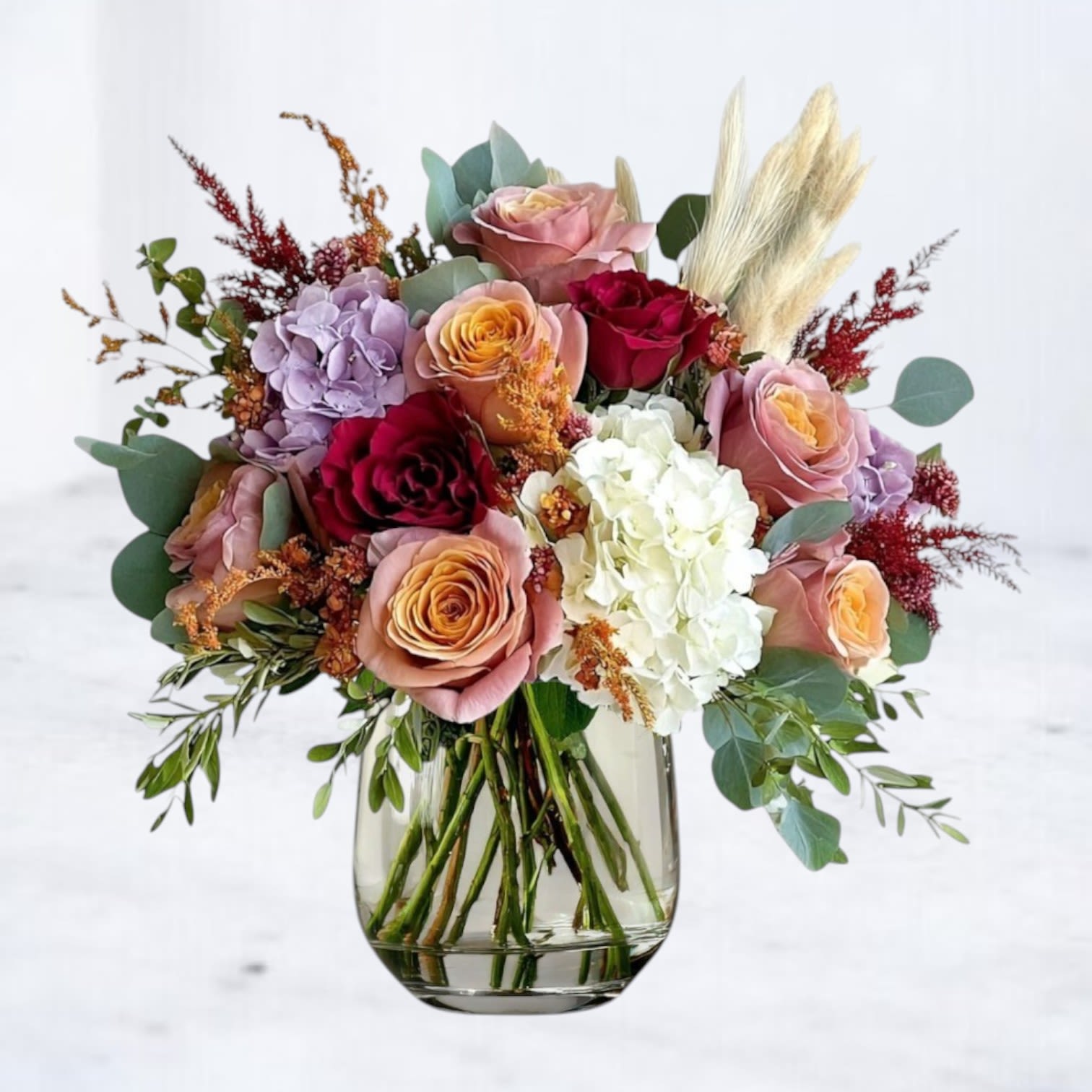 Autumn Horizon Autumn Horizon - The Autumn Horizon bouquet blends seasonal charm with timeless elegance. Featuring sunset-toned roses in peach, burgundy, and mauve, paired with ivory and lavender hydrangea, this design is accented with pampas grass, golden aster, and fresh greenery. Arranged in a sleek glass vase, it brings cozy sophistication to fall gatherings, Thanksgiving tables, or as a thoughtful seasonal gift. Available for same-day flower delivery in Houston and surrounding areas, this autumn-inspired bouquet captures the warmth and beauty of the season in every bloom.
