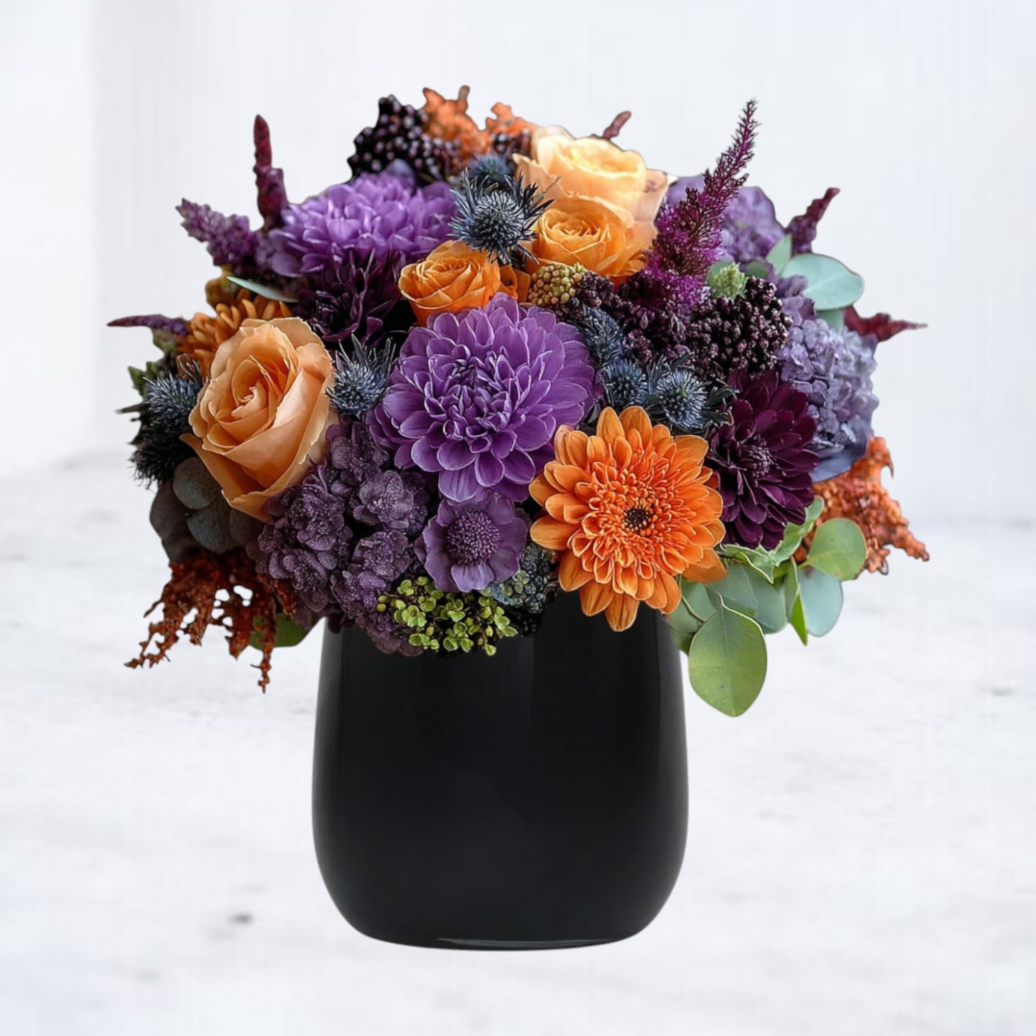Phantom Petals Phantom Petals - Phantom Petals is a strikingly elegant take on Halloween flowers, designed for those who want sophistication with seasonal flair. Featuring a dramatic palette of deep purple chrysanthemums, vivid orange roses and gerberas, purple hydrangea, indigo thistle, and rich seasonal textures, this bouquet is arranged in a sleek black vase for maximum impact. Perfect for Halloween parties, fall gatherings, or sending a bold autumn surprise, this arrangement blends mystery and luxury in every petal. Available for same-day delivery in Magnolia, The Woodlands, Conroe, Spring, Cypress, and greater Houston, it’s a gift that casts an unforgettable spell.