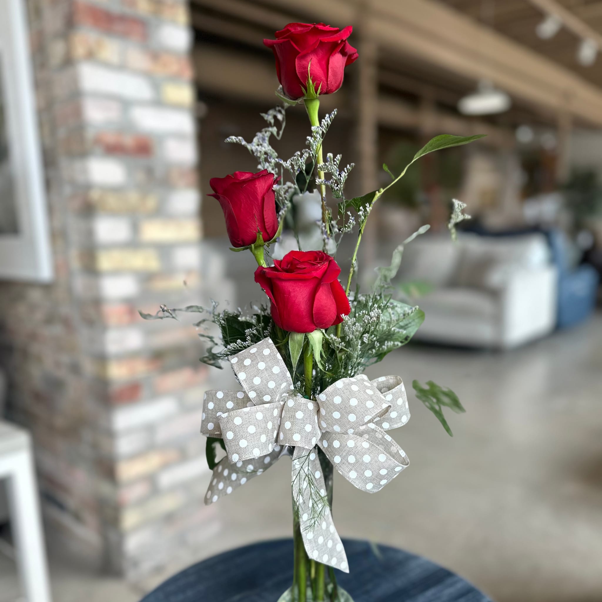 TRIO of LOVE Floral Arrangement by Birch &amp; Blossom  - A quiet expression that speaks volumes, TRIO of LOVE celebrates the timeless beauty of simplicity. Three elegant red roses stand side by side, each a symbol of devotion, kindness, and respect. Delicate filler blooms and a hand-tied bow complete the design, creating a gesture that feels as sincere as it looks.  One rose for love, one for the charity of your heart, and one for the esteem you carry for another, together, they form a story of affection that needs no words.  Handcrafted in-house at Birch &amp; Blossom, TRIO of LOVE is perfect for sending joy, marking milestones, or adding a vivid pop of beauty to any space.