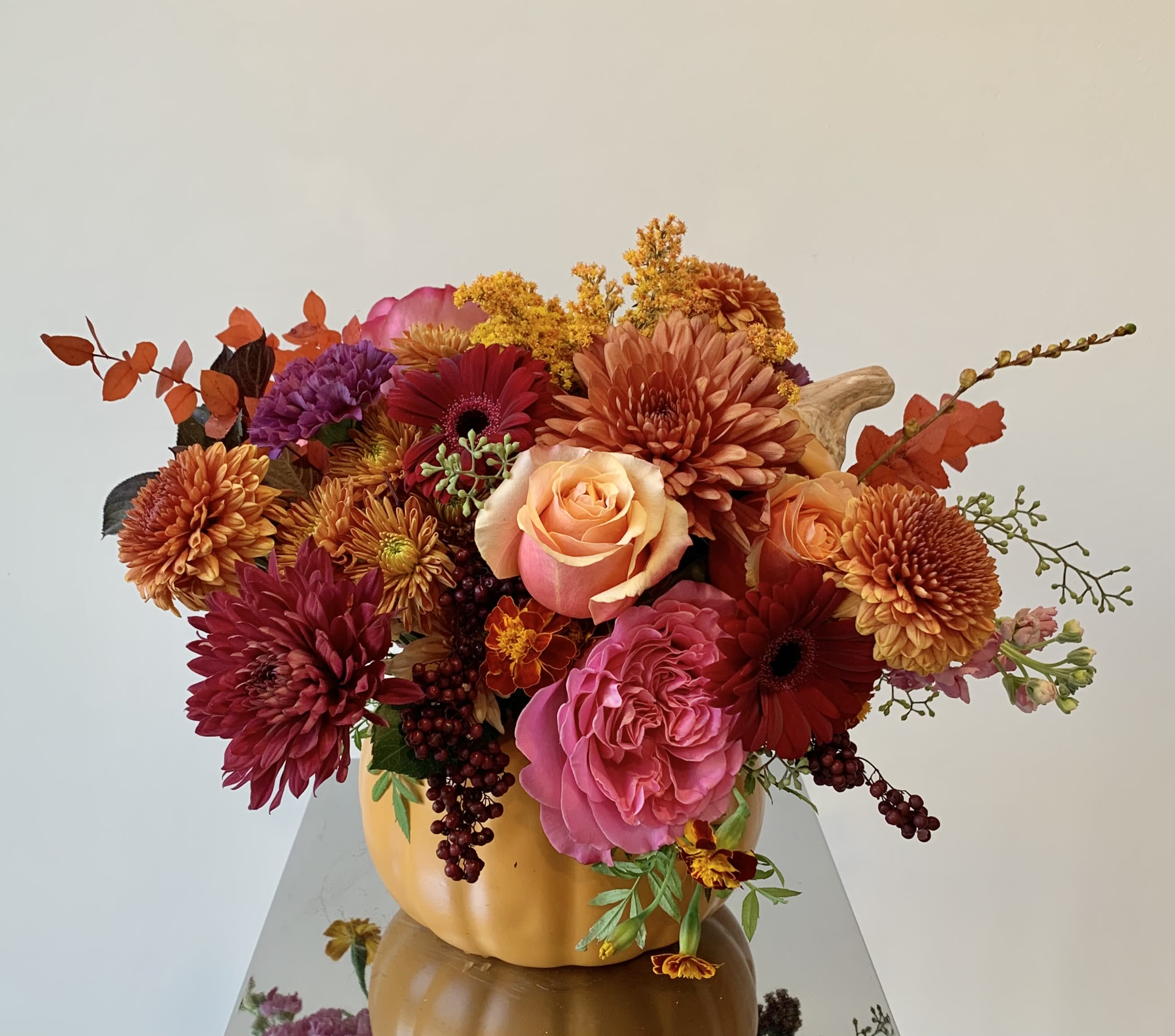Flower Pumpkin Flower Pumpkin - A foam-free, lush flower arrangement in a ceramic orange pumpkin in a vibrant autumn color palette with a mix of premium flowers such as roses, ranunculus, cremons, disbuds, gerber daisies, berries, and other unique flower fillers and seasonal foliage right in texture. Colors may vary.