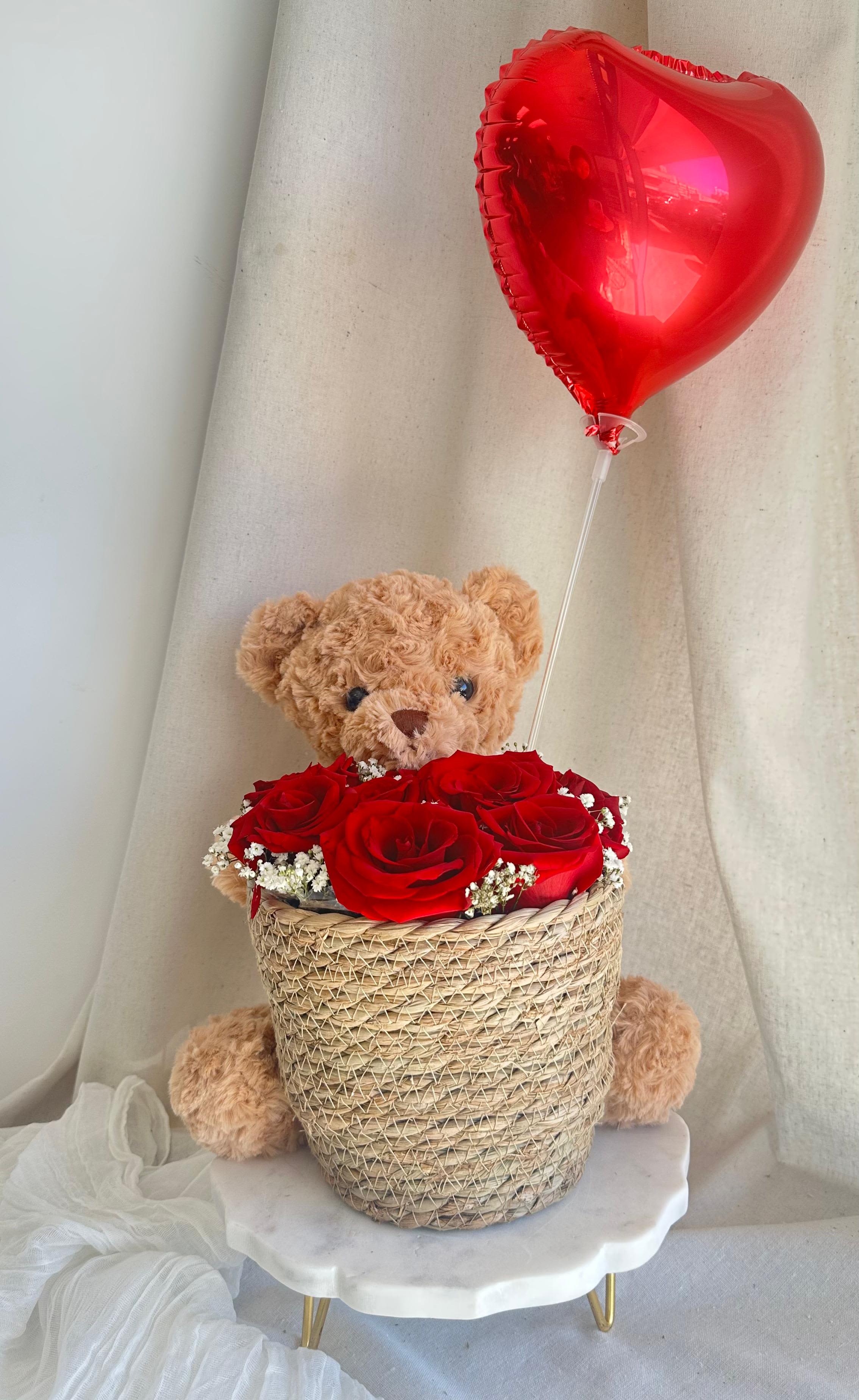 Love and Cuddle in Red  - A gift set featuring a basket with roses and baby's breath, plus a plush teddy bear and a foil balloon.   Flower types may vary depending on the season.