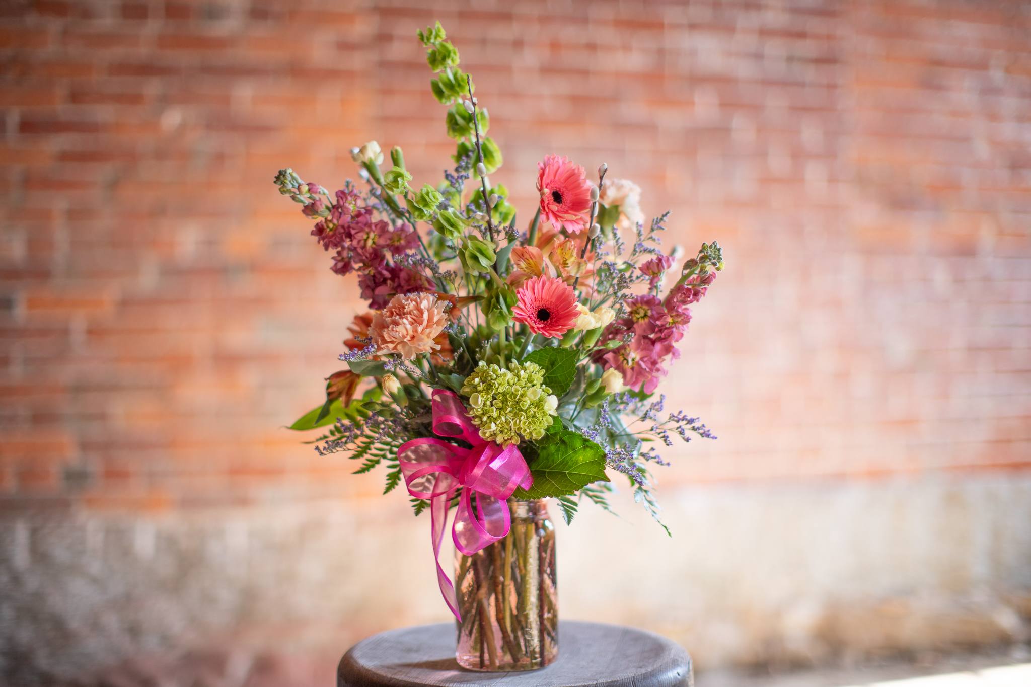 Ina's Garden - A wildflower mix in a textured glass vase. This mix of standard and premium grade florals is perfection. Glassware may be assorted in color or clear. Focal flowers will include playful gerbera daisy and hydrangea. The linear floral varieties may vary, photo shows bells of Ireland and stock. Other tall flower varieties could include delphinium, snapdragon or larkspur. Colors will vary based on glassware. Zach created this design, he is quite the fan of the Barefoot Contessa.
