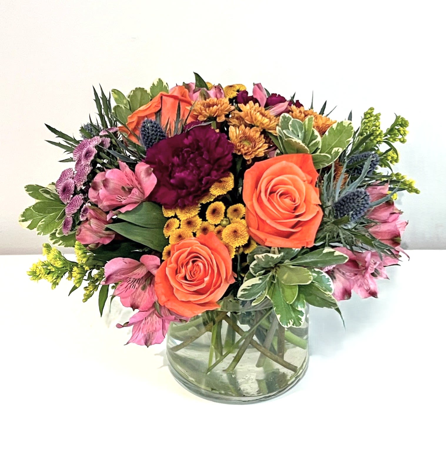 Warm Embrace - This fall foliage inspired bouquet is sure to bring warm &amp; cozy feelings to anyone that receives it. The freshest selection of blooms in seasonal autumn colors are arranged low and compact &amp; delivered in a short clear glass cylinder. It's the perfect gift to send for any occasion.    Measures approx. 10&quot; tall x 10&quot; wide Orientation: All around 