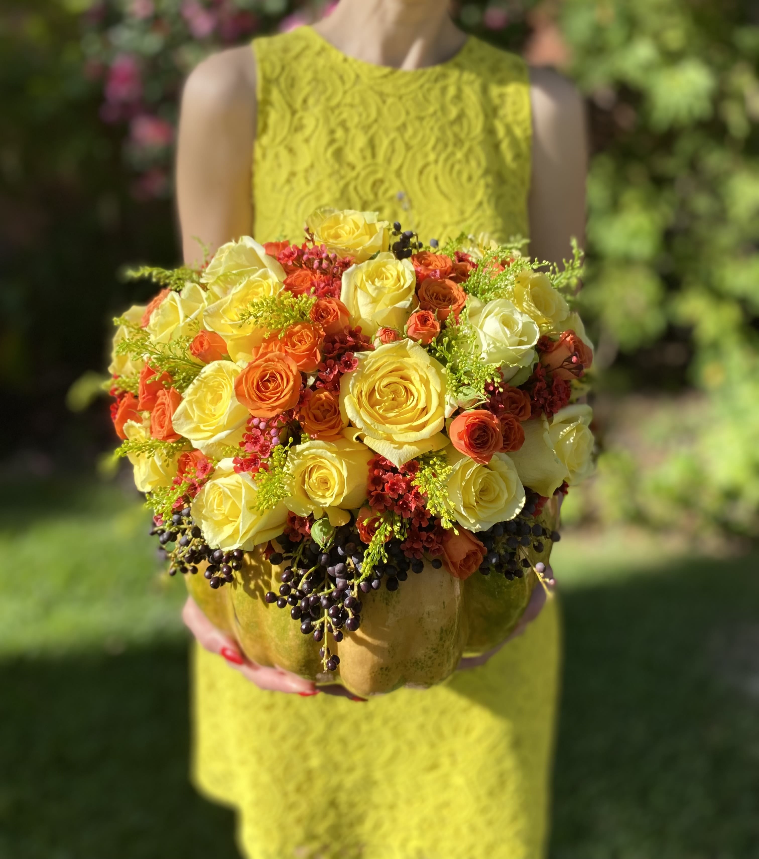 87D- Pumpkin Blooms - This enchanting arrangement features a mix of lush roses, delicate spray roses, and fresh greenery, all beautifully nestled inside a real pumpkin. The rich textures and warm hues create a stunning autumn display, perfect for adding a touch of seasonal elegance to any setting. DELUXE size is shown in the picture.