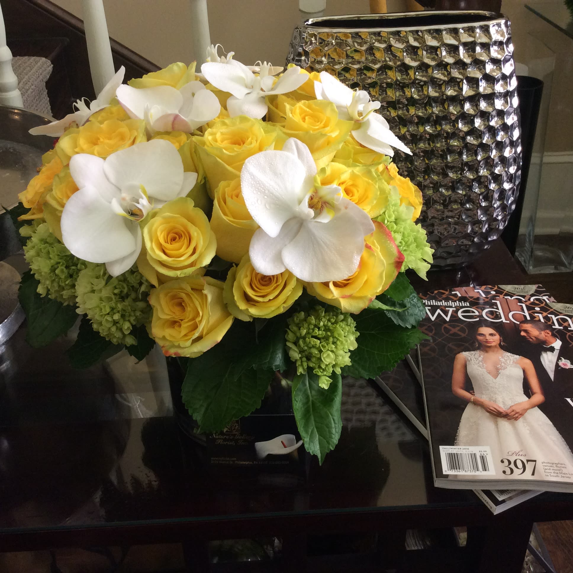 Sunshine roses and orchids - Yellow roses accented by elegant white orchids with golden lips arranged artistically by the expert hands of our designers. May request different color for the rose in the special instructions: we'll do our best to accommodate.  Starting size is smaller desk top size, upgrades provide larger sizes with more blossoms and stems.