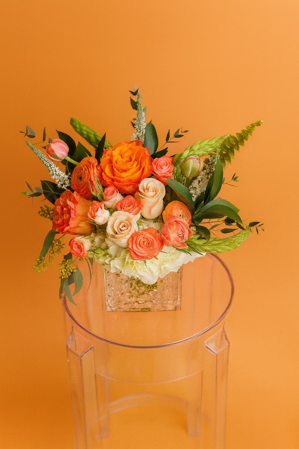 Pumpkin Spice Blooms - Warm and inviting, this autumn arrangement features lush orange and peach roses, ranunculus, and creamy accents that capture the cozy charm of fall. Designed in a modern glass vase, it’s the perfect way to add a seasonal glow to any home or celebration.